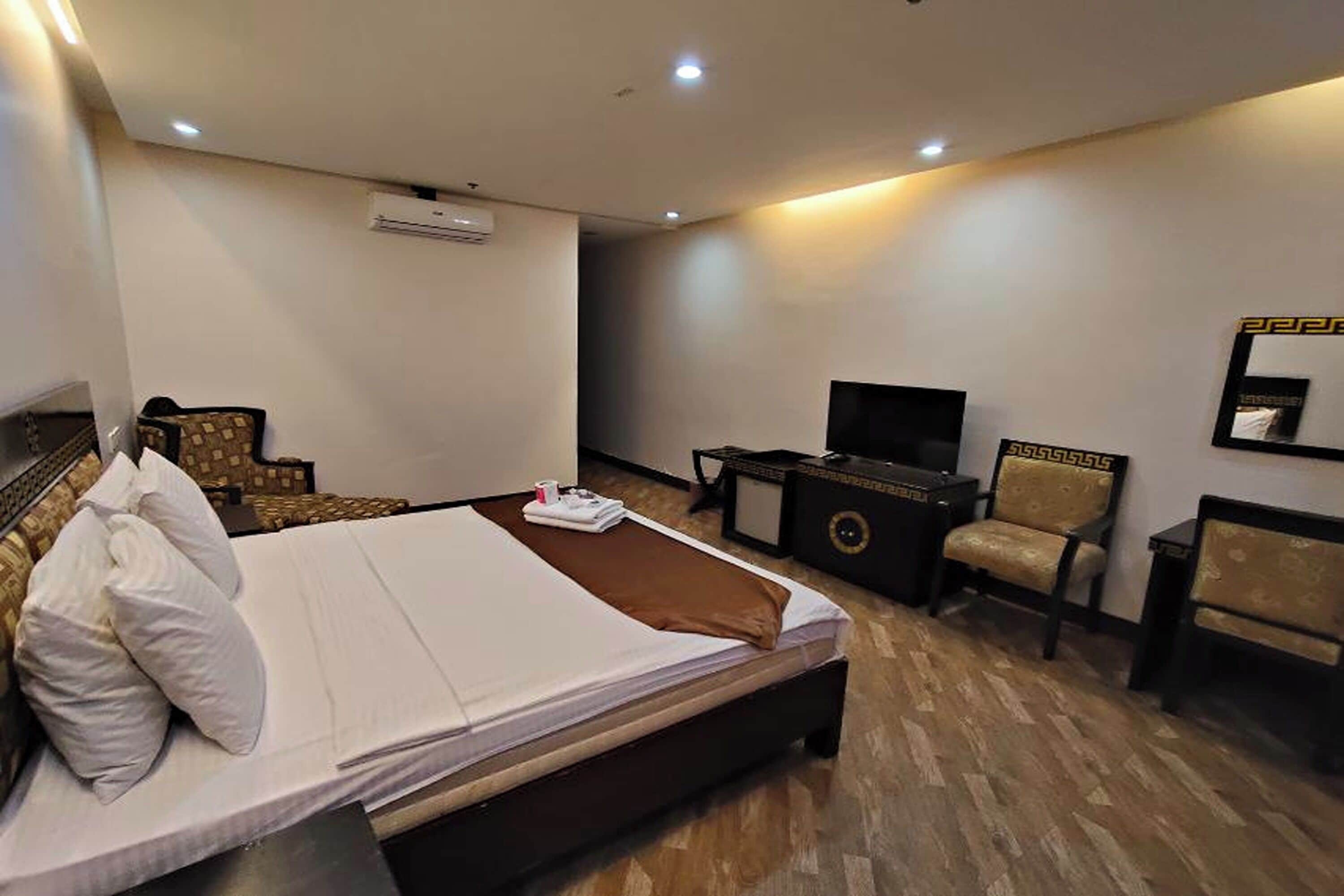 A hotel room with a bed, a TV, a desk, and two chairs.
