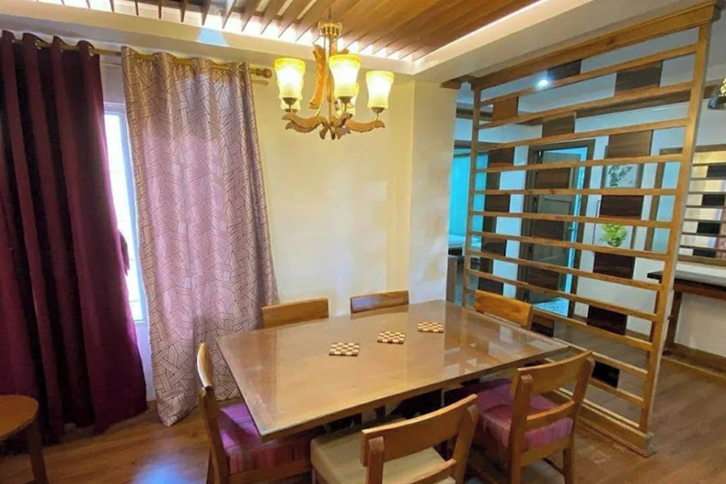 A dining area with a wooden table and chairs, a chandelier, and a decorative partition with glass blocks.