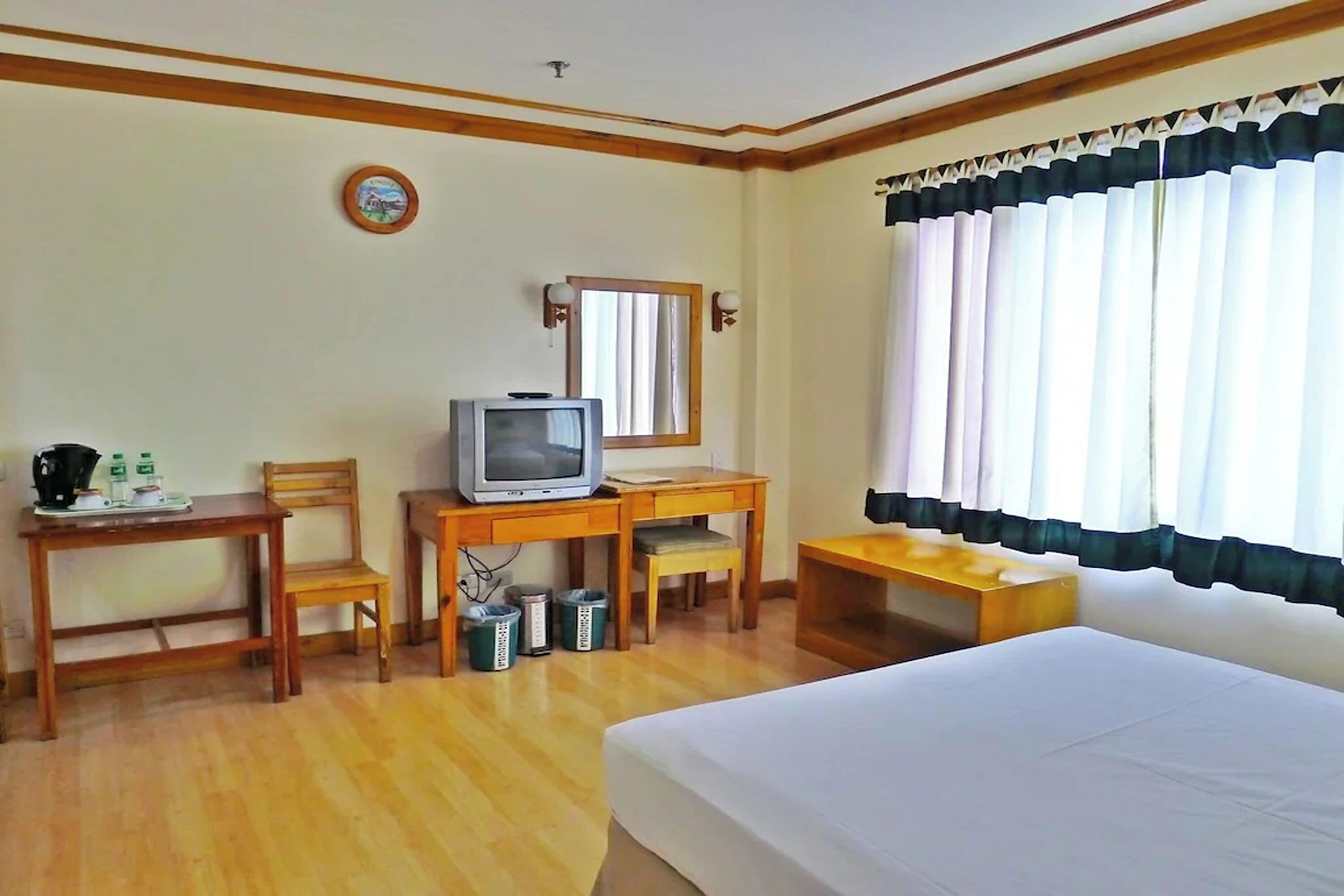 Ein Hotelzimmer mit Bett, Schreibtisch mit Fernseher, Stuhl, kleinem Tisch und einem Fenster mit Vorhängen.