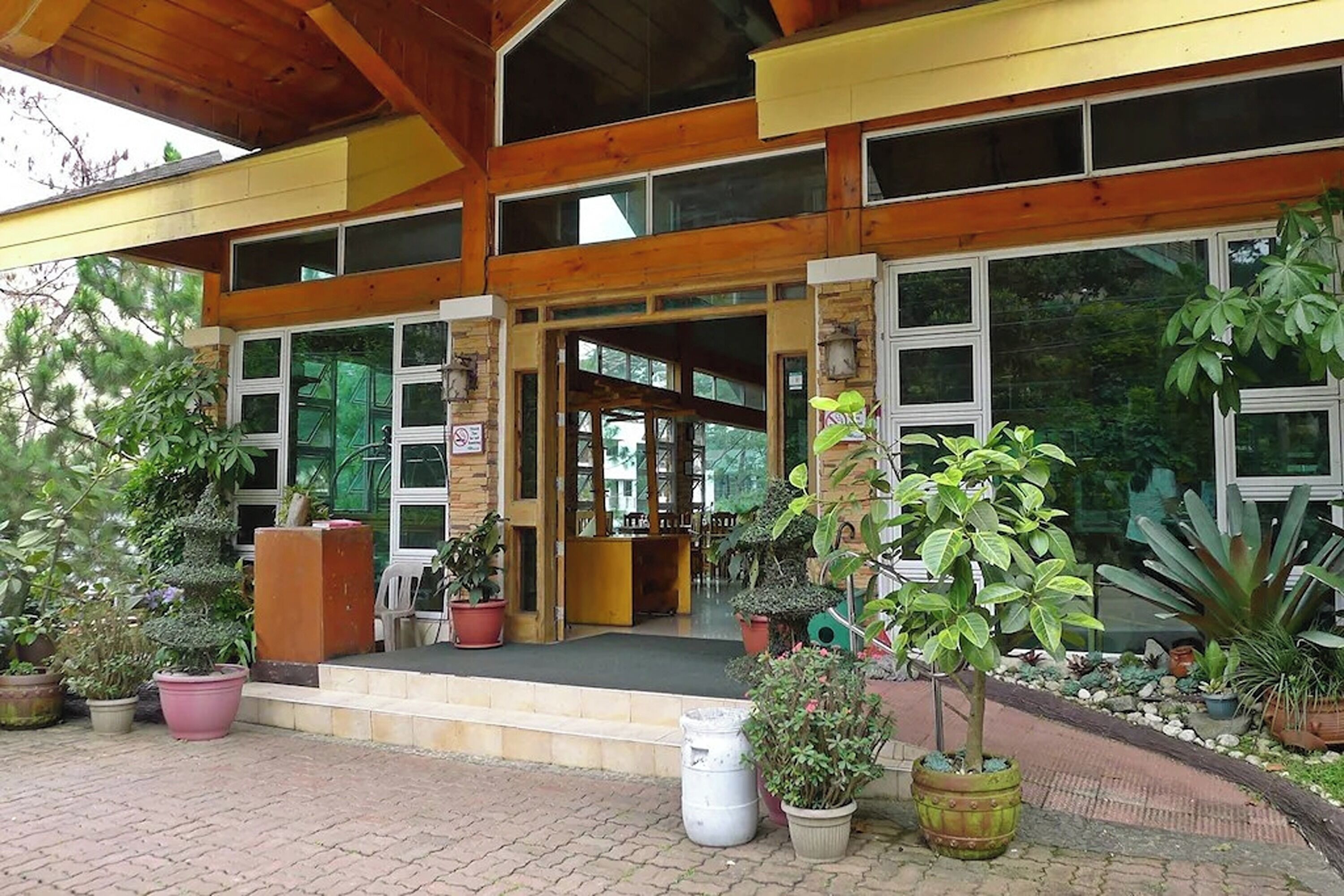 A two-story building with a wooden facade, large windows, and a covered entrance area with potted plants.