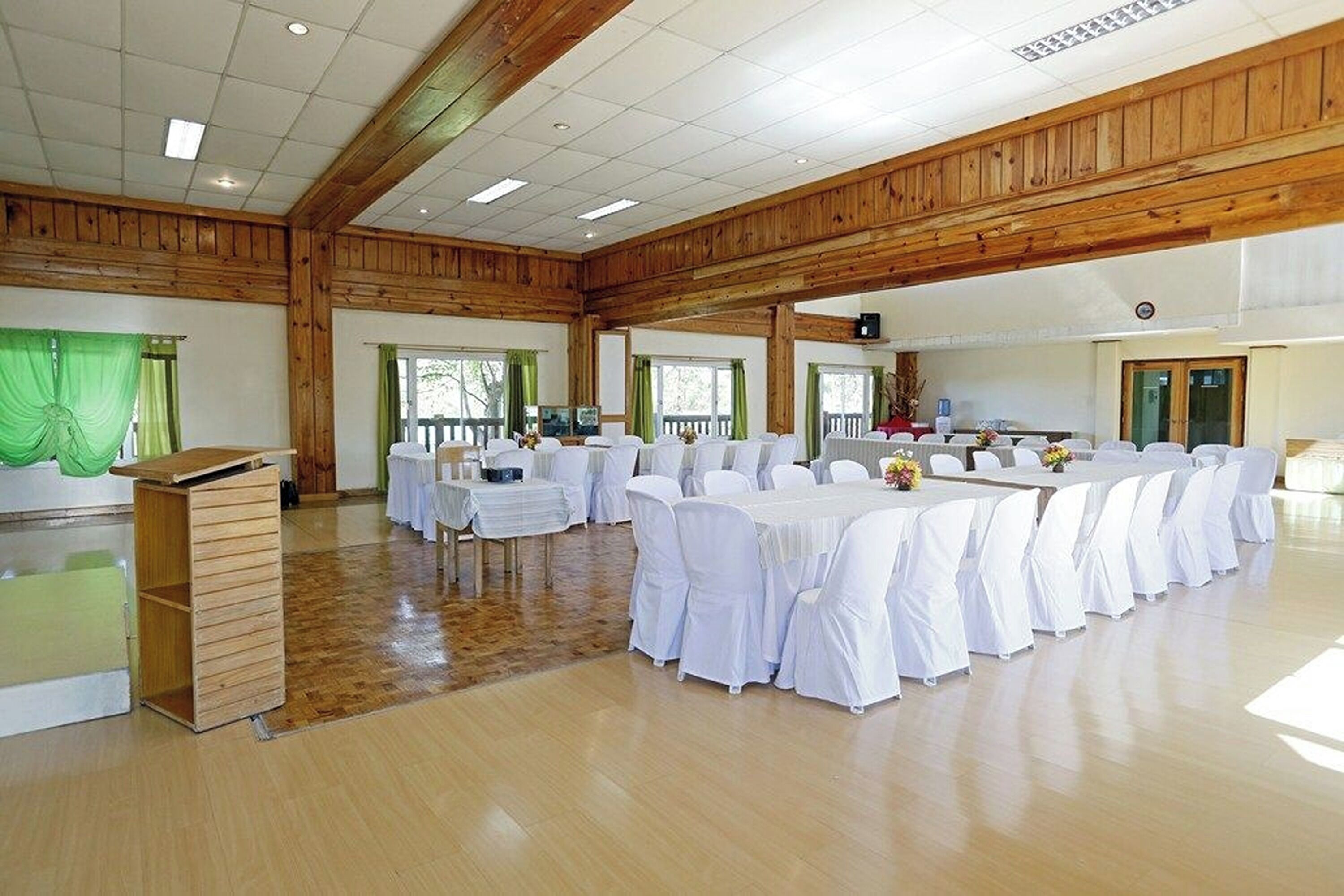 A large hall with wooden beams, white tables with chairs, and a podium.