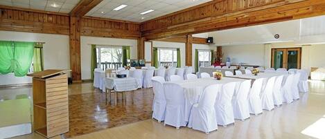 A large hall with wooden beams, white tables with chairs, and a podium.