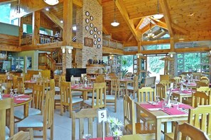 A spacious dining area with wooden tables and chairs, a stone wall with clocks, and large windows offering a view of the outdoors. - Ridgewood Hotel Baguio Near The Mansion (Baguio)