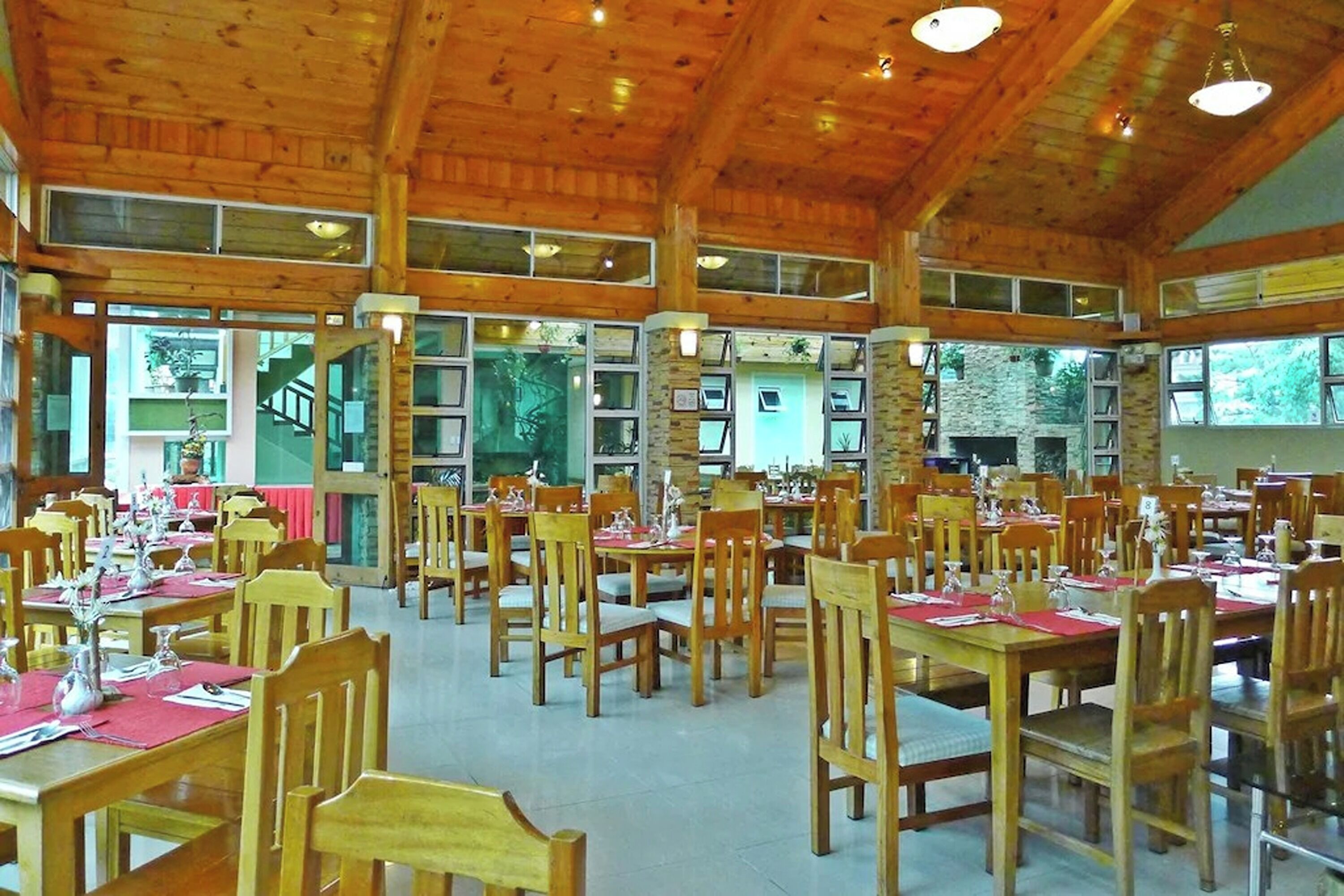 A spacious dining area with wooden tables and chairs, large windows, and a stone wall.