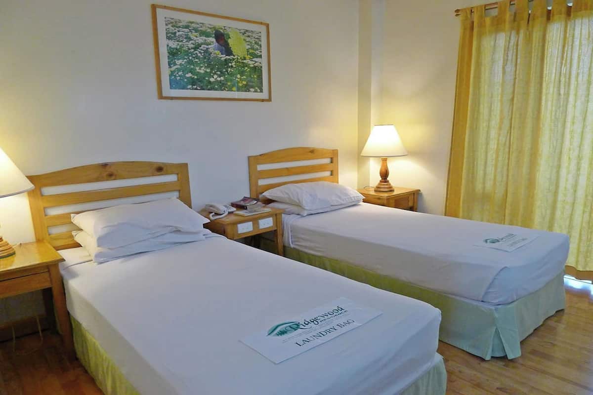 A hotel room with two single beds, a bedside table with a lamp, a framed picture on the wall, and a curtain.