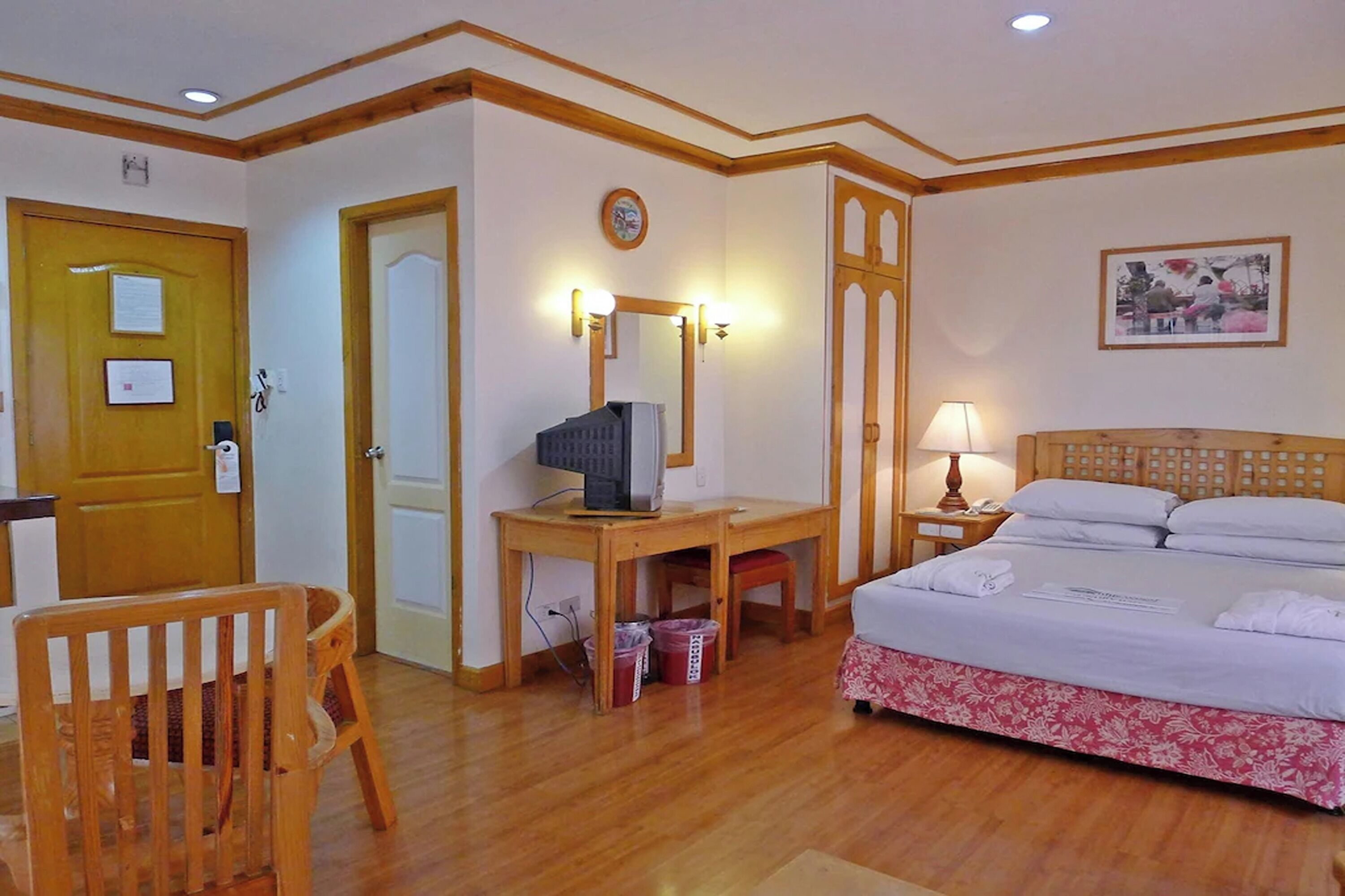 Habitación de hotel con escritorio de madera, cama con ropa blanca, una silla de madera y una cama con cabecera y estructura de madera.