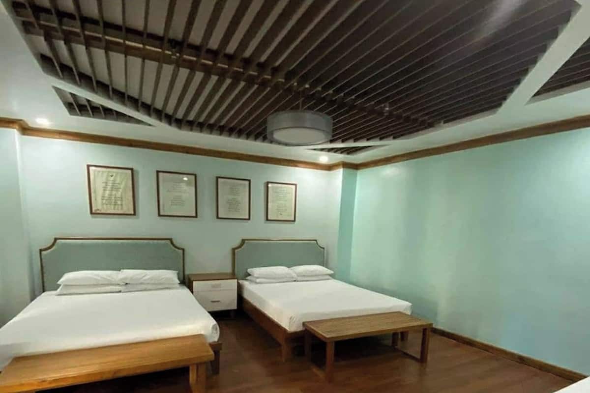 A hotel room with two single beds, a wooden bench, a nightstand, and framed certificates on the wall.
