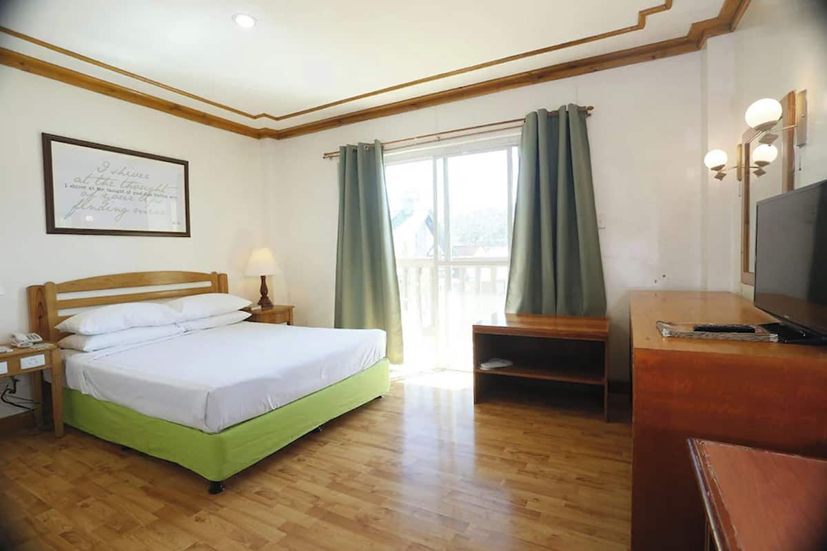 A hotel room with a bed, a desk, a television, and a window with curtains.