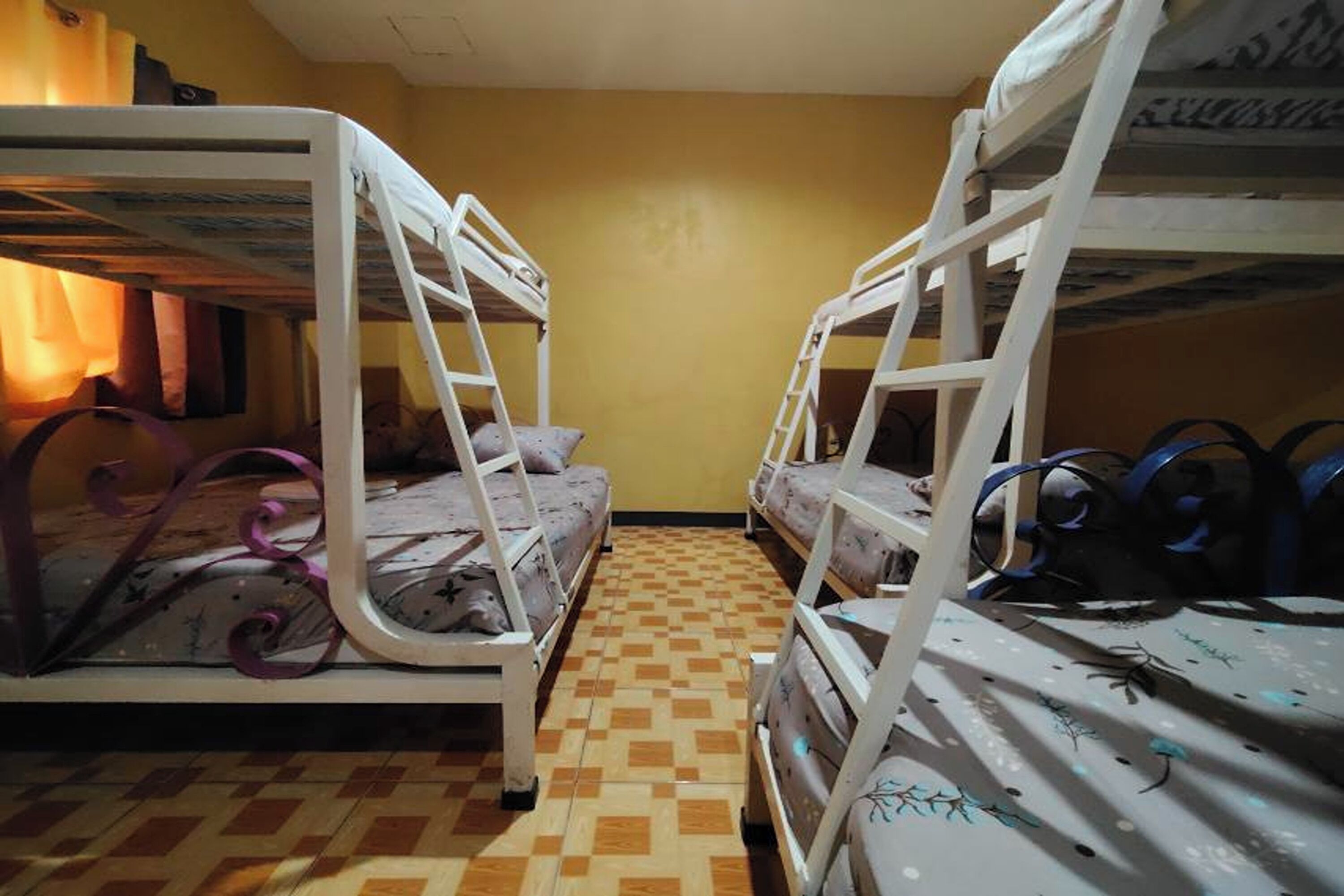 A dormitory room with bunk beds, a checkered floor, and a plain yellow wall.