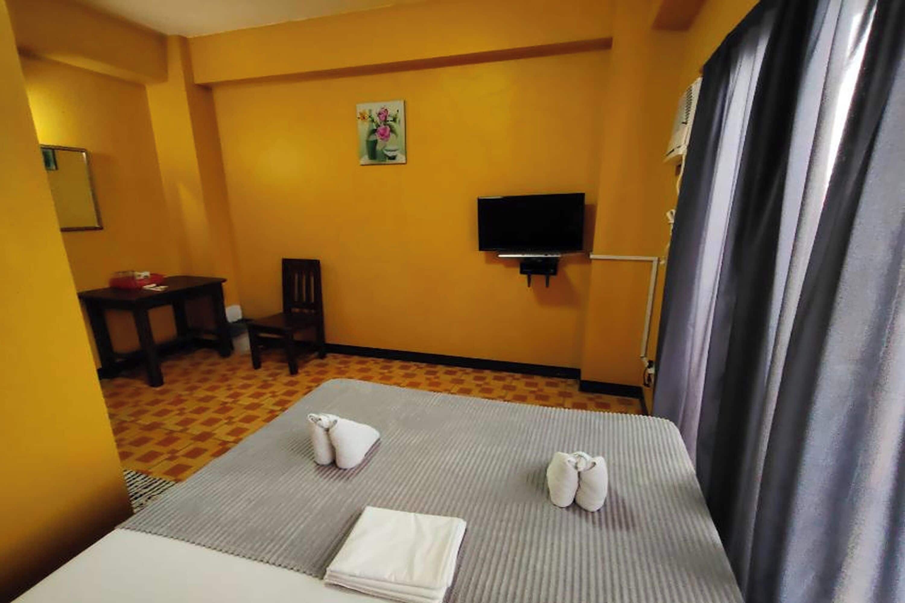 A hotel room with a bed, a TV mounted on the wall, a chair, and a small table with a vase of flowers.
