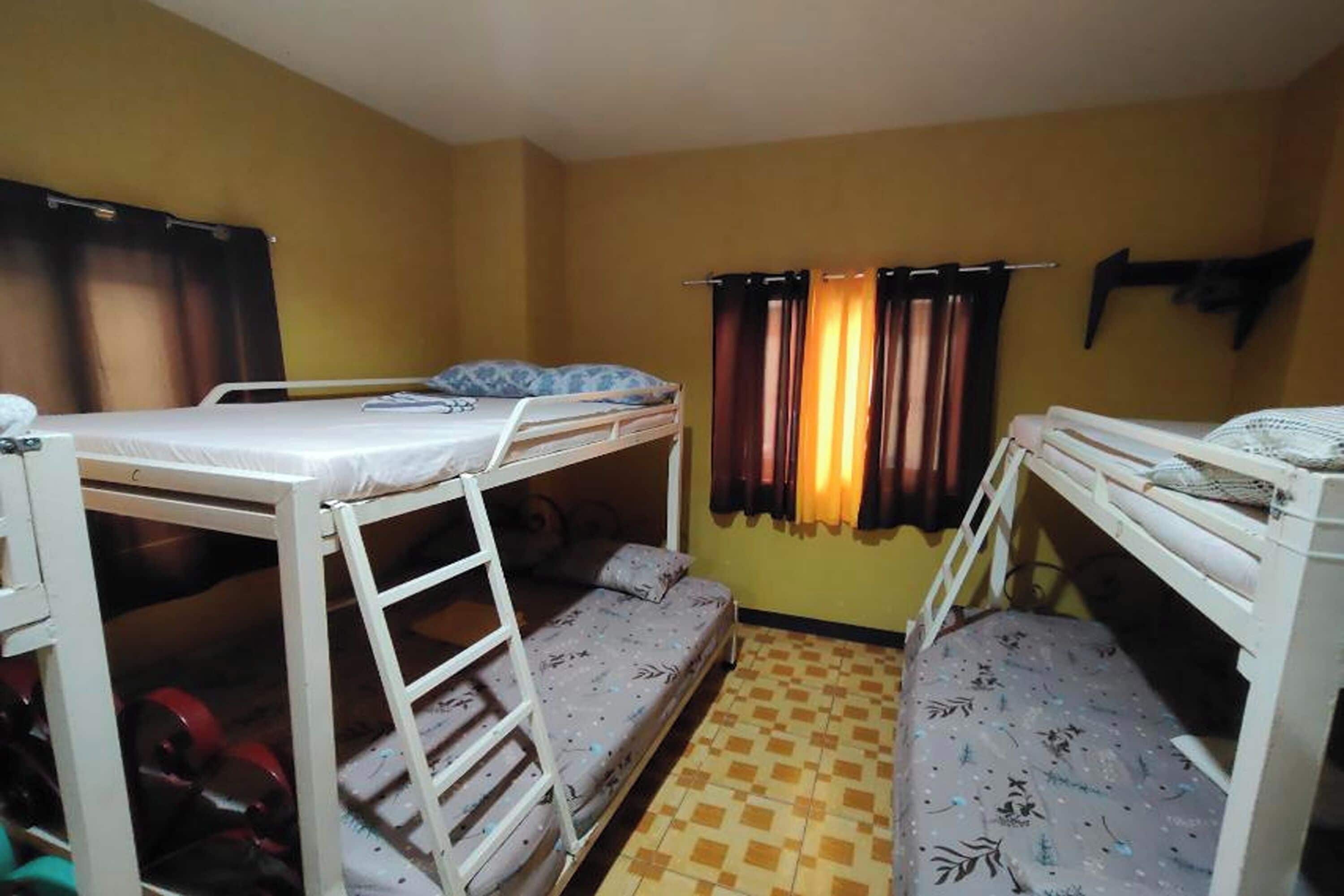 A dormitory room with bunk beds, a window with curtains, and a tiled floor.