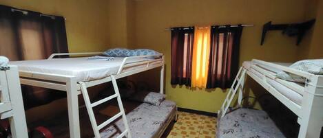 A dormitory room with bunk beds, a window with curtains, and a tiled floor.