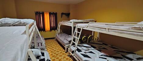 A dormitory room with bunk beds, a patterned floor, and a window with curtains.