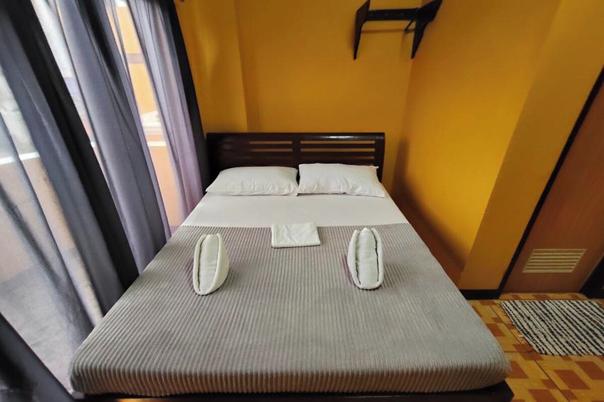 A neatly made bed with a grey mattress and white pillows, a wooden headboard, and a window with curtains.