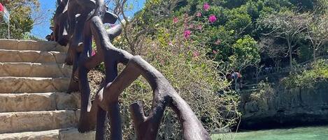 Uma escadaria com grades de metal abstratas e originais, que dá acesso a uma área verde exuberante e com águas cristalinas.