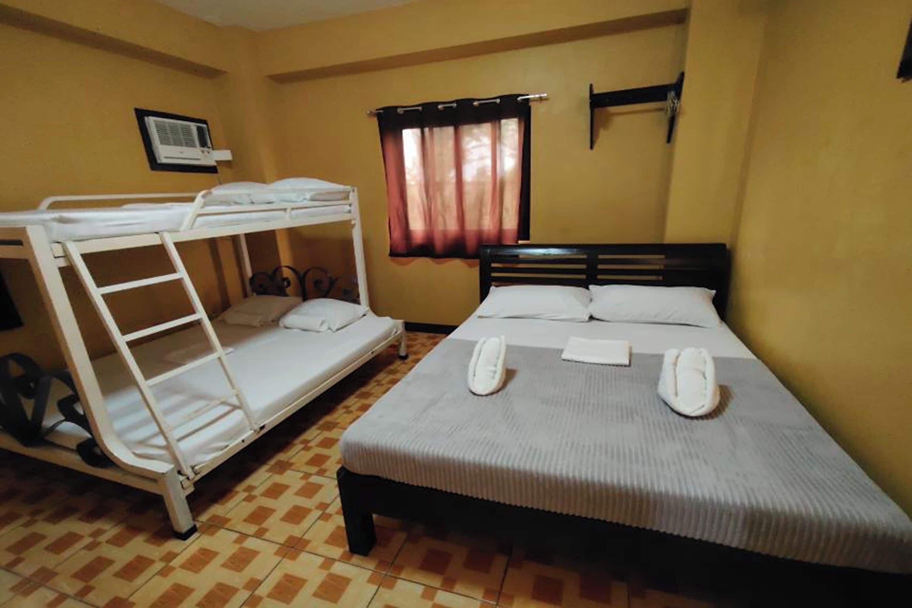 A room with a bunk bed, a single bed, a window with curtains, and an air conditioning unit on the wall.