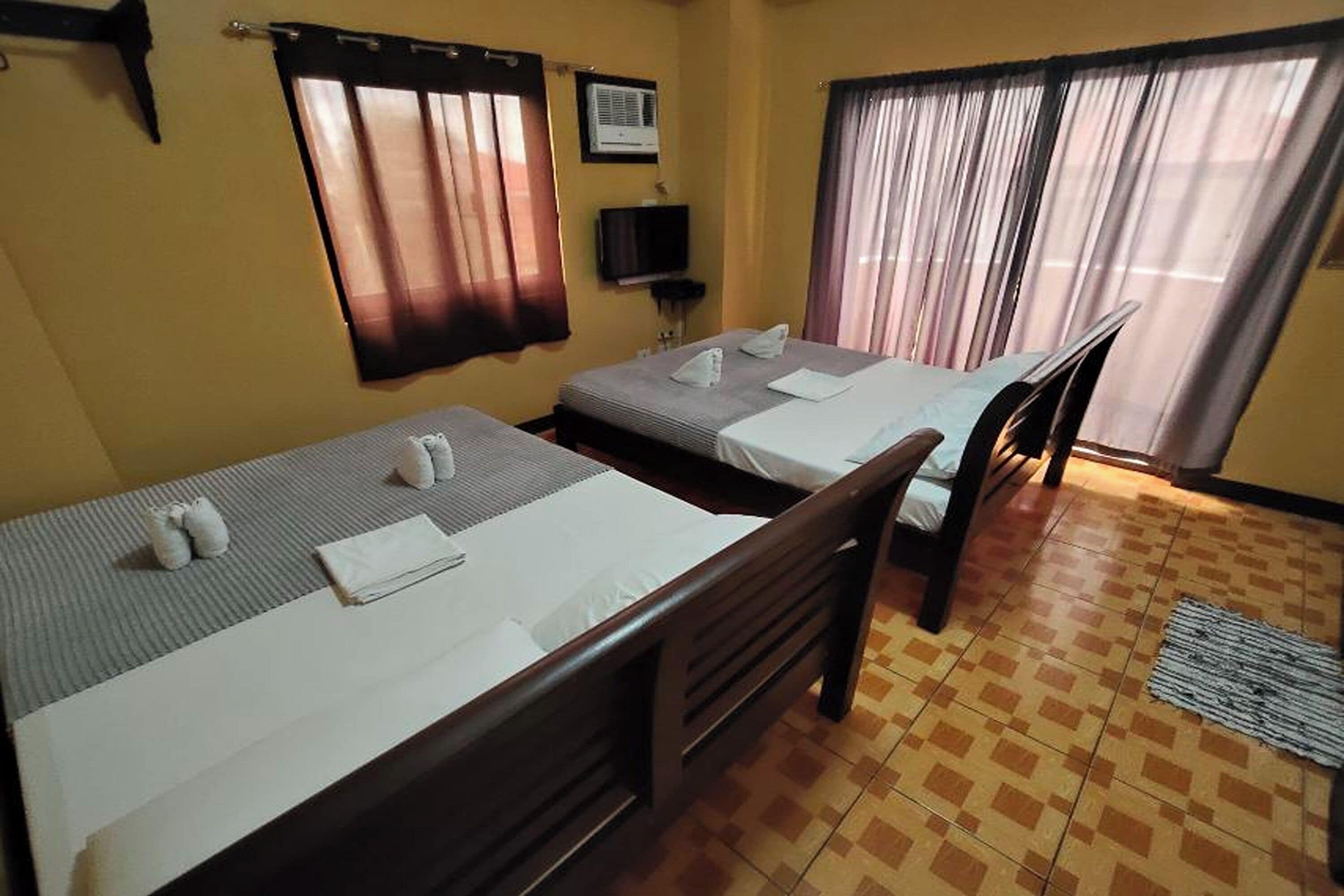 Una habitación de hotel con dos camas individuales, una silla de madera, un televisor y una ventana con cortinas.