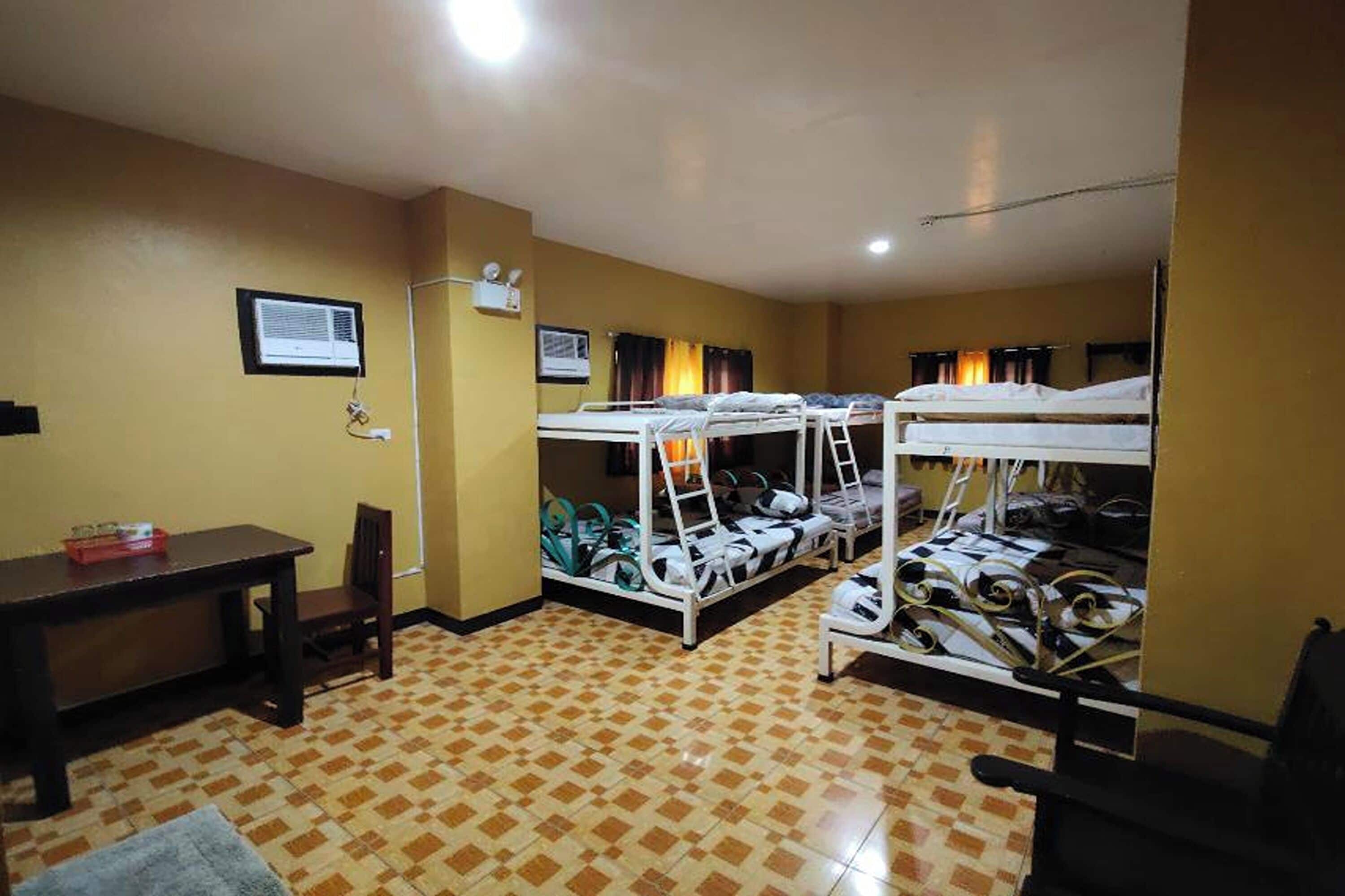 A dormitory room with bunk beds, a desk, and a chair.