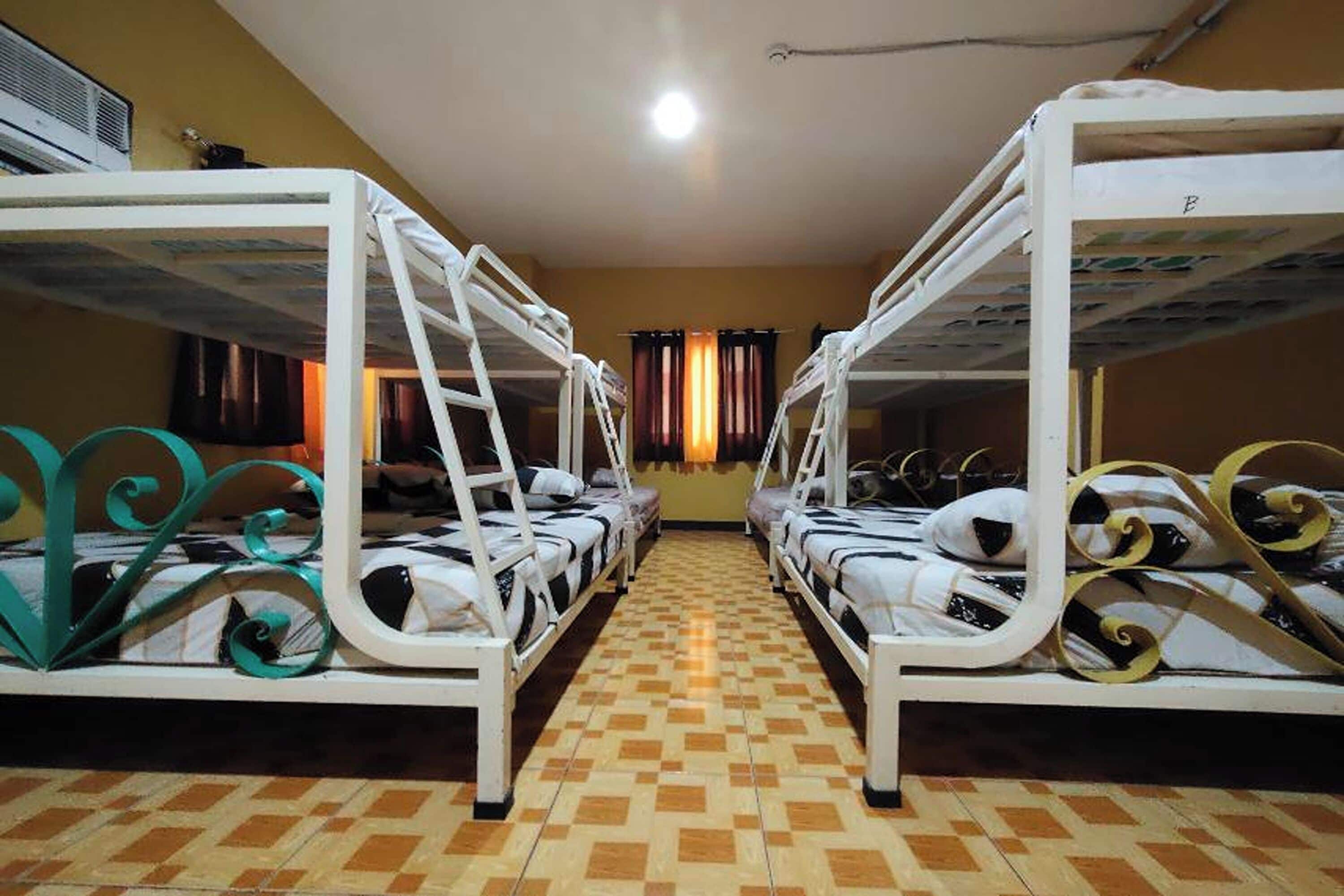 Une chambre de dortoir avec des lits superposés, un sol carrelé et une fenêtre avec des rideaux.
