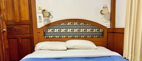 Camera d'albergo con porta in legno, un letto con copripiumino blu, due asciugamani arrotolati e una testiera con motivo decorativo.