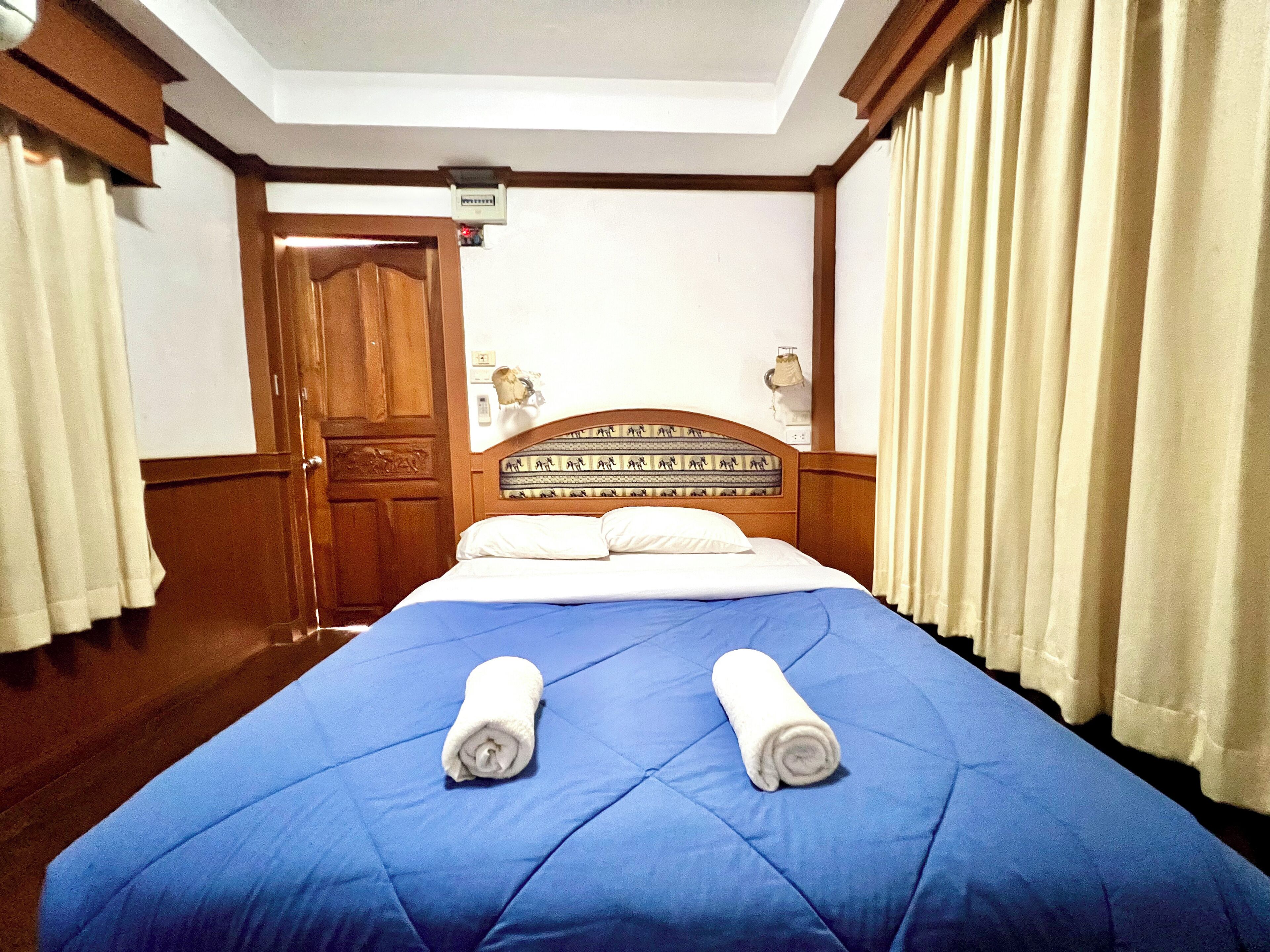 Une chambre d’hôtel avec un grand lit, une tête de lit en bois et deux serviettes enroulées posées sur le lit.