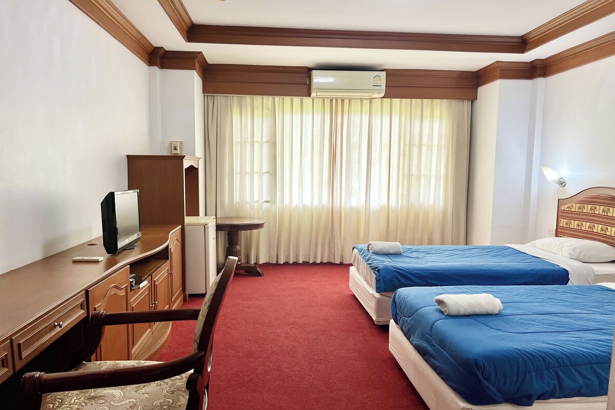 Une chambre d’hôtel avec deux lits, un bureau avec une télévision, une chaise, une petite table et un appareil de climatisation.