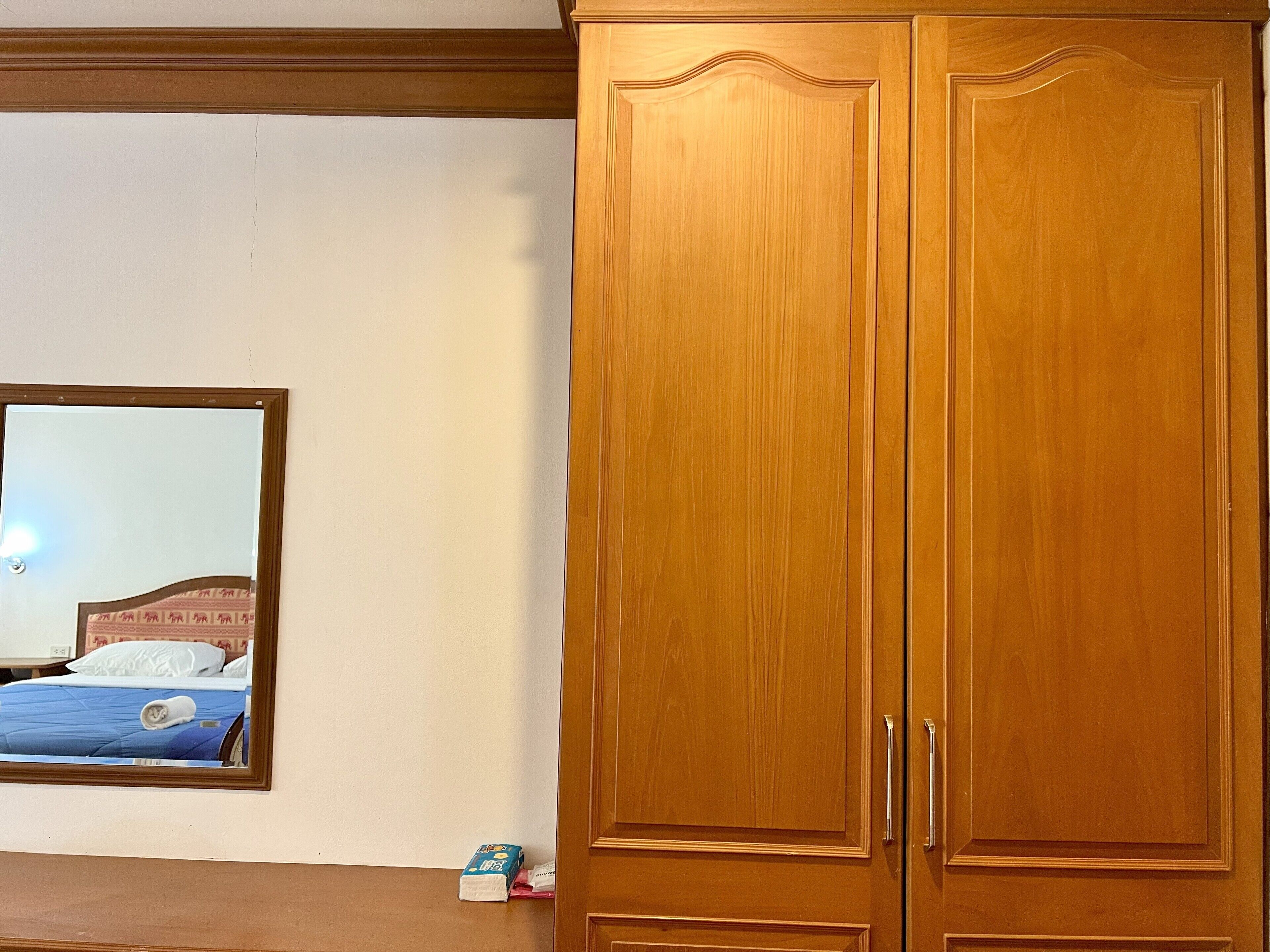 A bedroom with a wooden wardrobe, a mirror on the wall, and a bed with a blue bedspread.