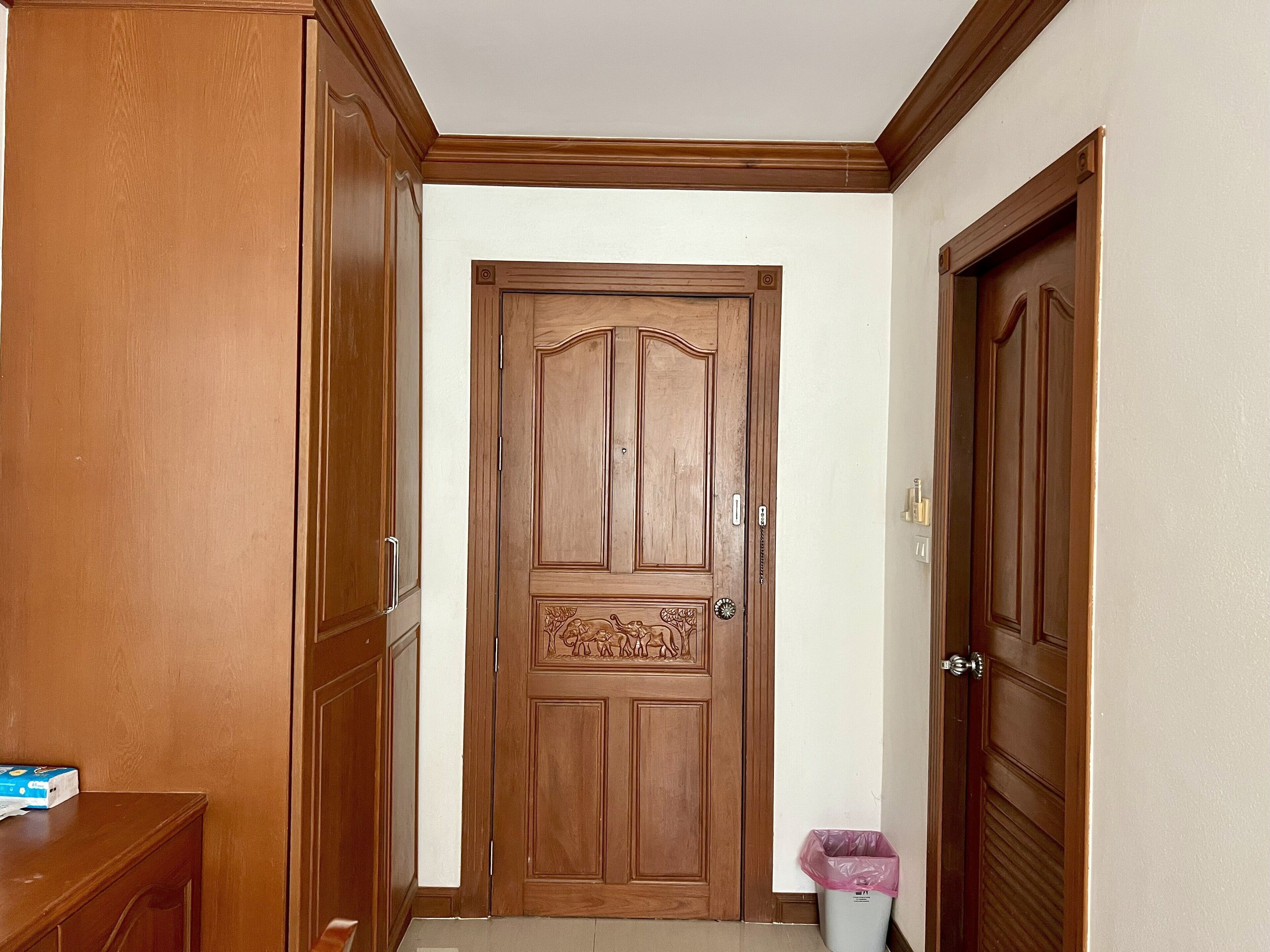 A hallway with a wooden door, a trash bin, and a wooden cabinet.