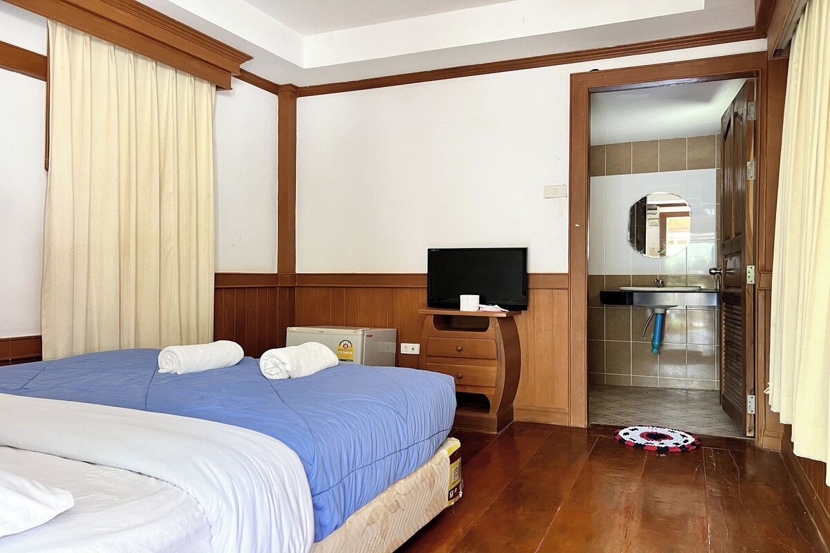 Une chambre d’hôtel avec un grand lit, une télévision, un petit bureau et une salle de bain visible à travers une porte ouverte.