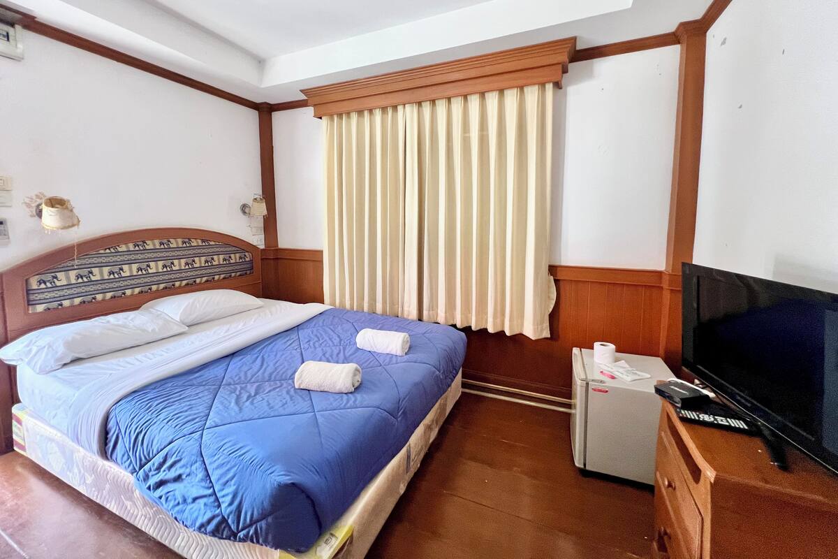 Quarto de hotel com cama, televisão e pequena mesa com frigorífico.