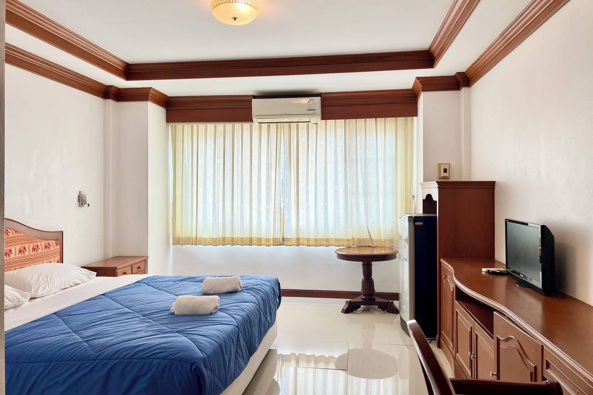 Quarto de hotel com cama, televisão, mesa pequena e janela com cortinas.