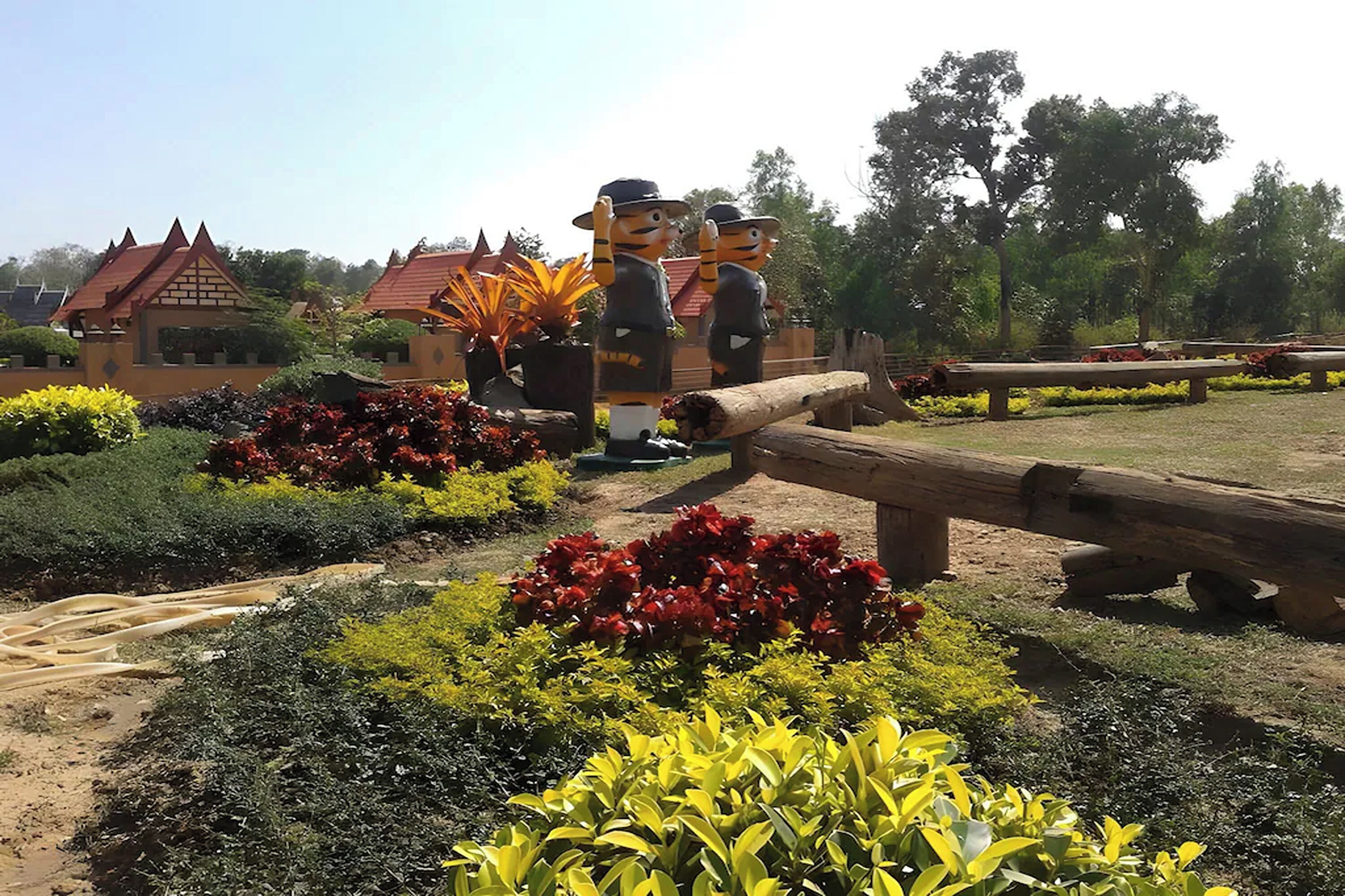 Un jardín con estatuas, un puente de madera y un edificio con techo rojo.