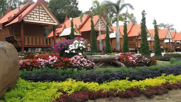 Una hilera de edificios tradicionales de madera con tejados rojos, rodeada de macizos de flores de colores y vegetación.