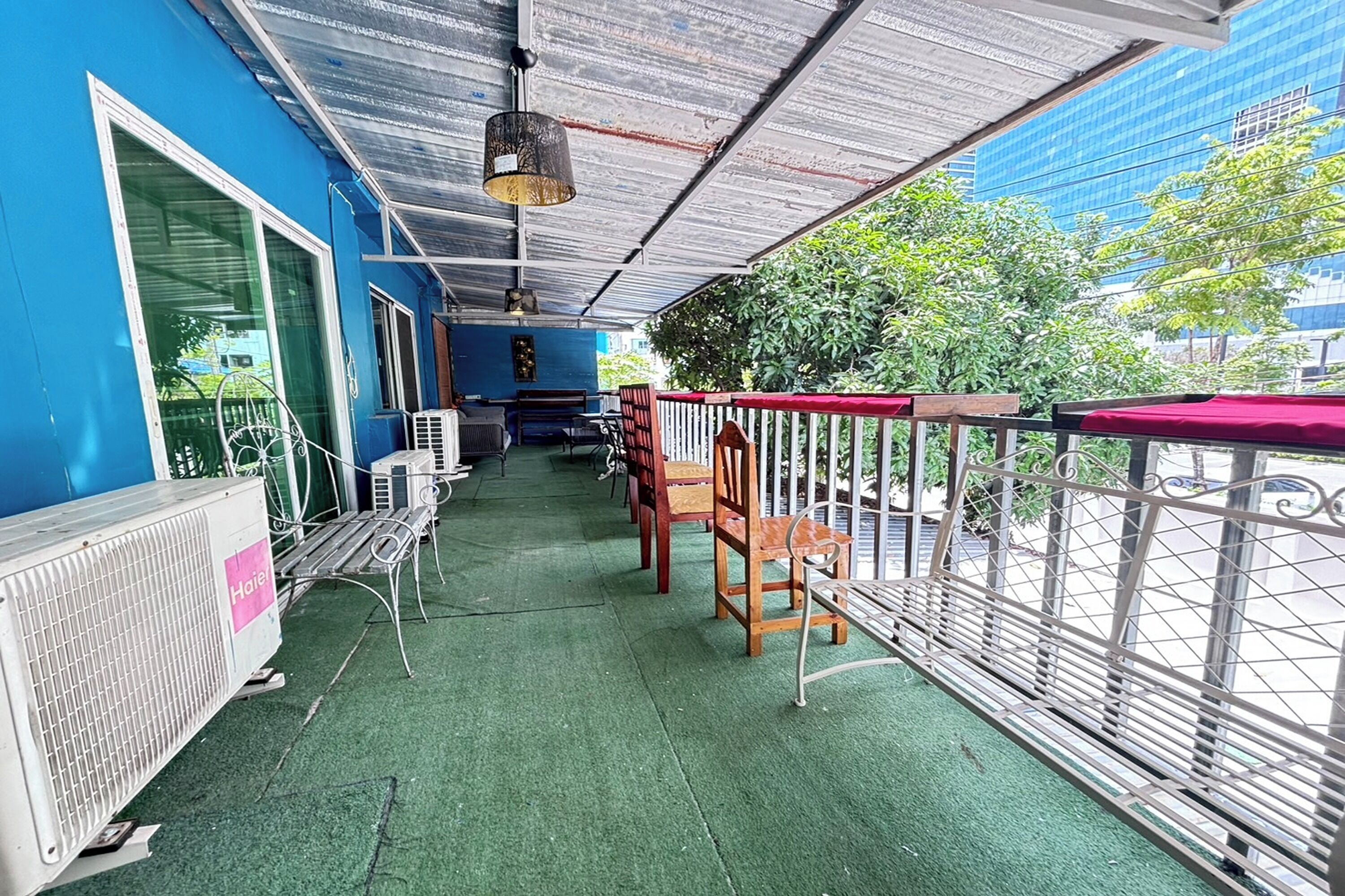 A covered outdoor seating area with green flooring, metal railings, and a view of a blue building.
