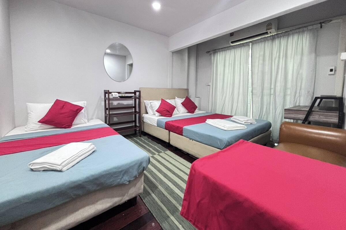 A hotel room with three beds, a mirror, a desk, and a window with curtains.