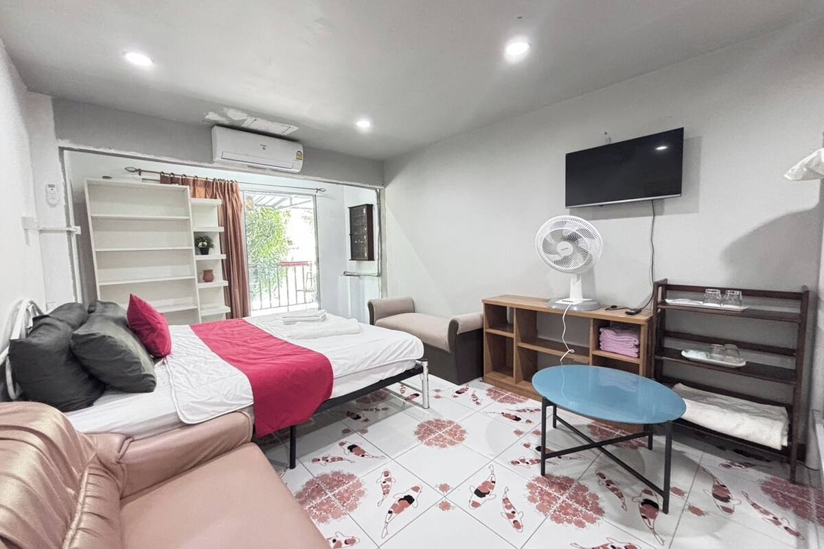 A hotel room with a bed, a sofa, a TV, a fan, and a window with curtains.