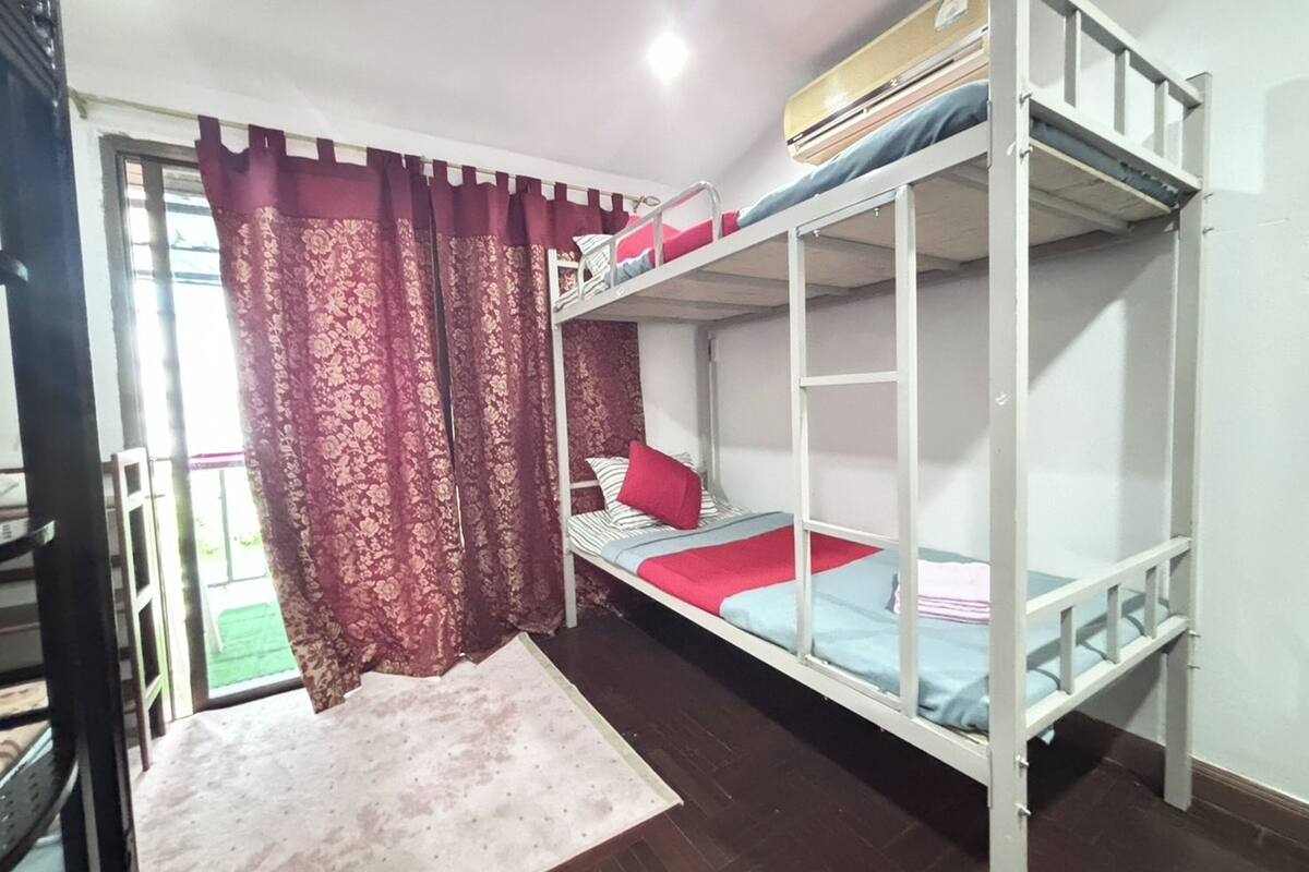 A dormitory room with bunk beds, a window with curtains, and a small table.