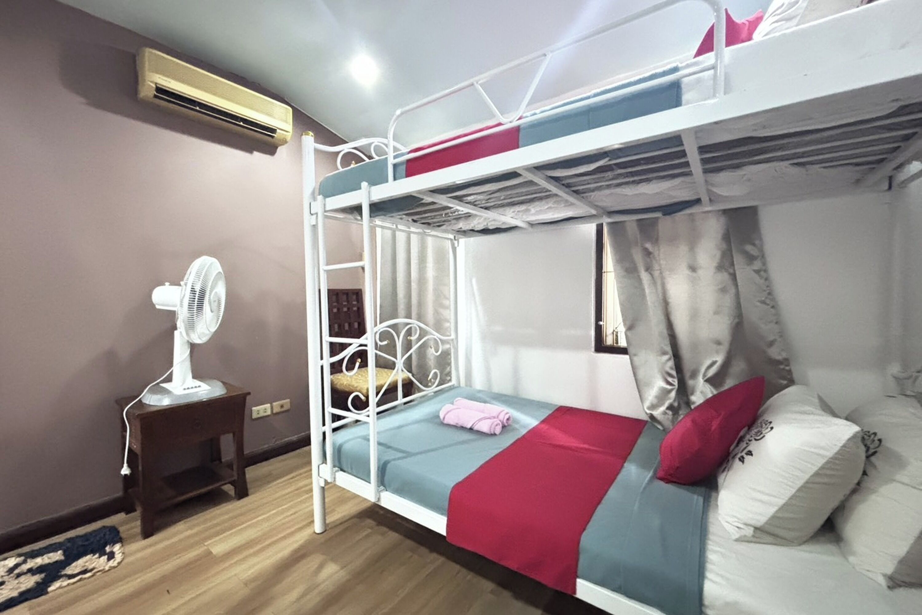 A bunk bed room with a fan, a small table, and a window with curtains.