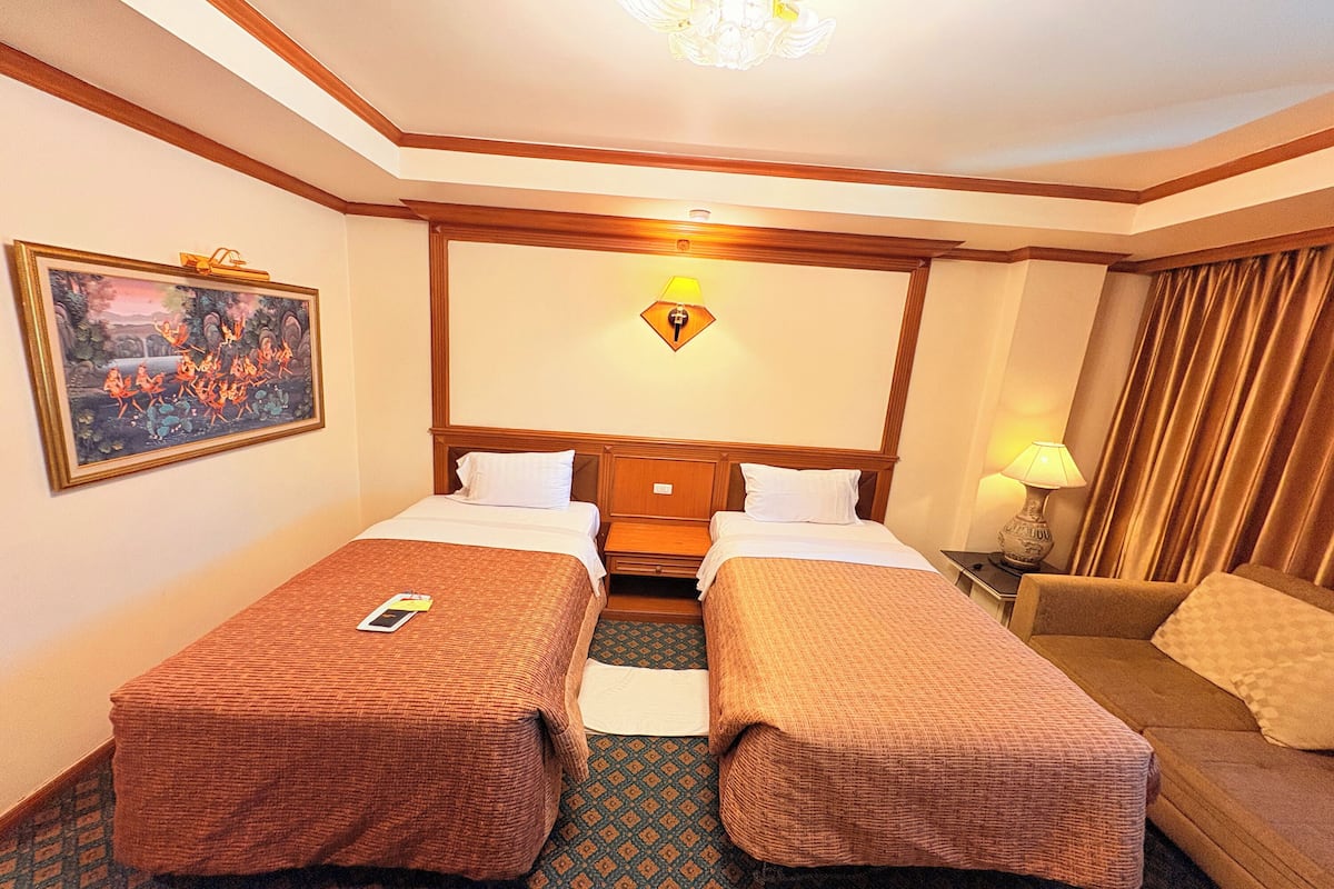Habitación de hotel con dos camas individuales, un sofá, un cuadro en la pared y una lámpara en la mesita de noche.