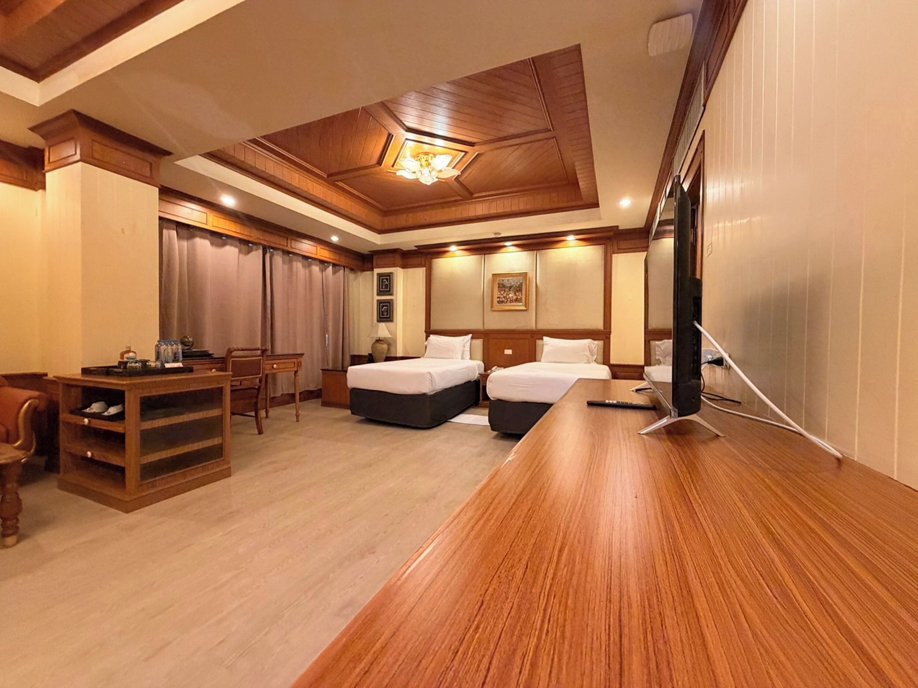 A hotel room with two beds, a desk, a chair, a TV, and a ceiling light fixture.