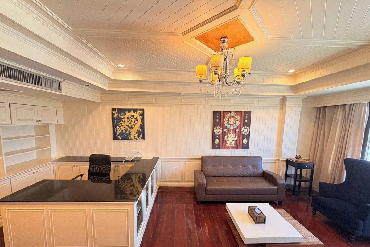 A hotel room with a kitchenette, a sofa, a coffee table, and a chandelier.