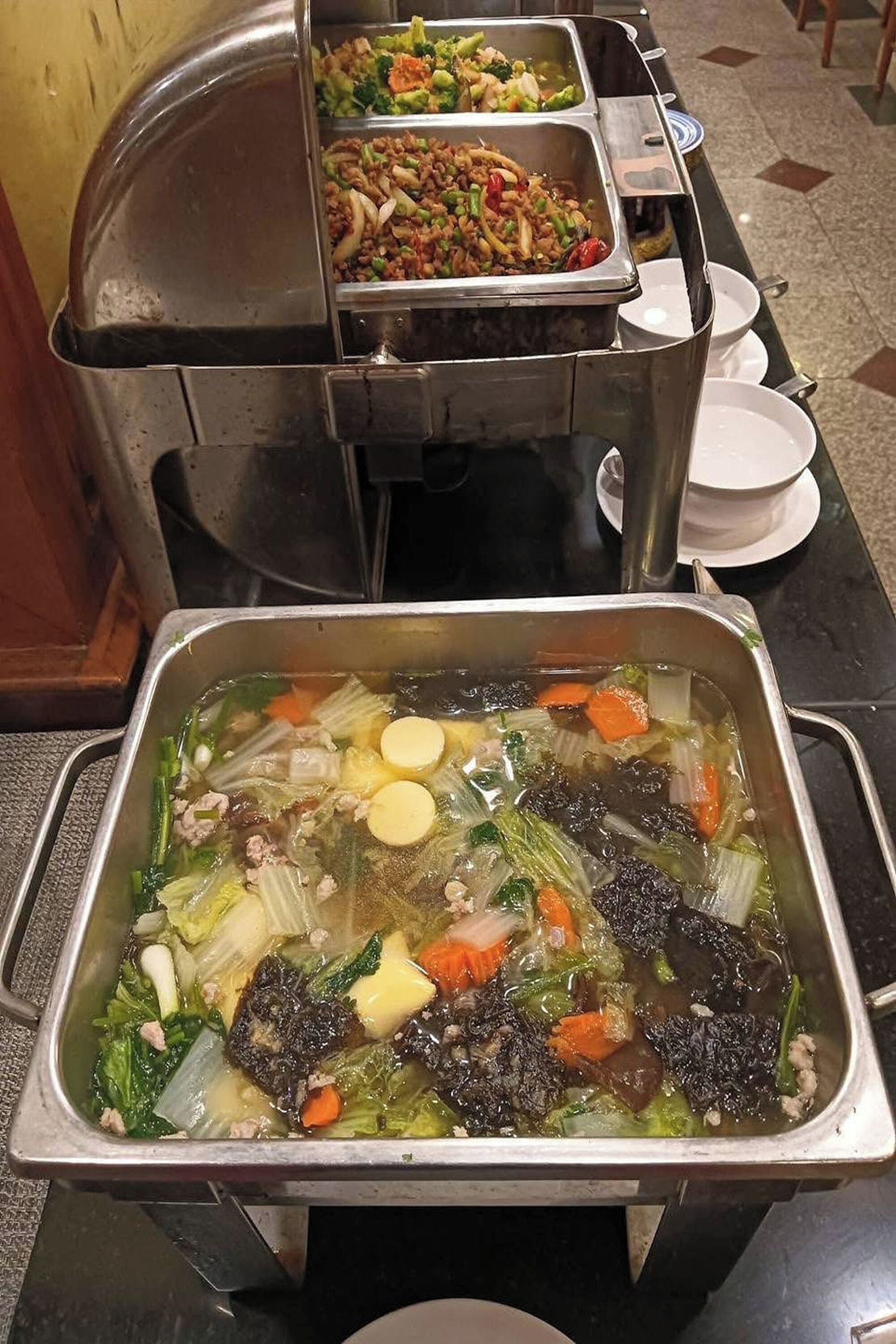 A buffet with various dishes including a soup with vegetables and meat, a stir-fry, and other prepared foods.