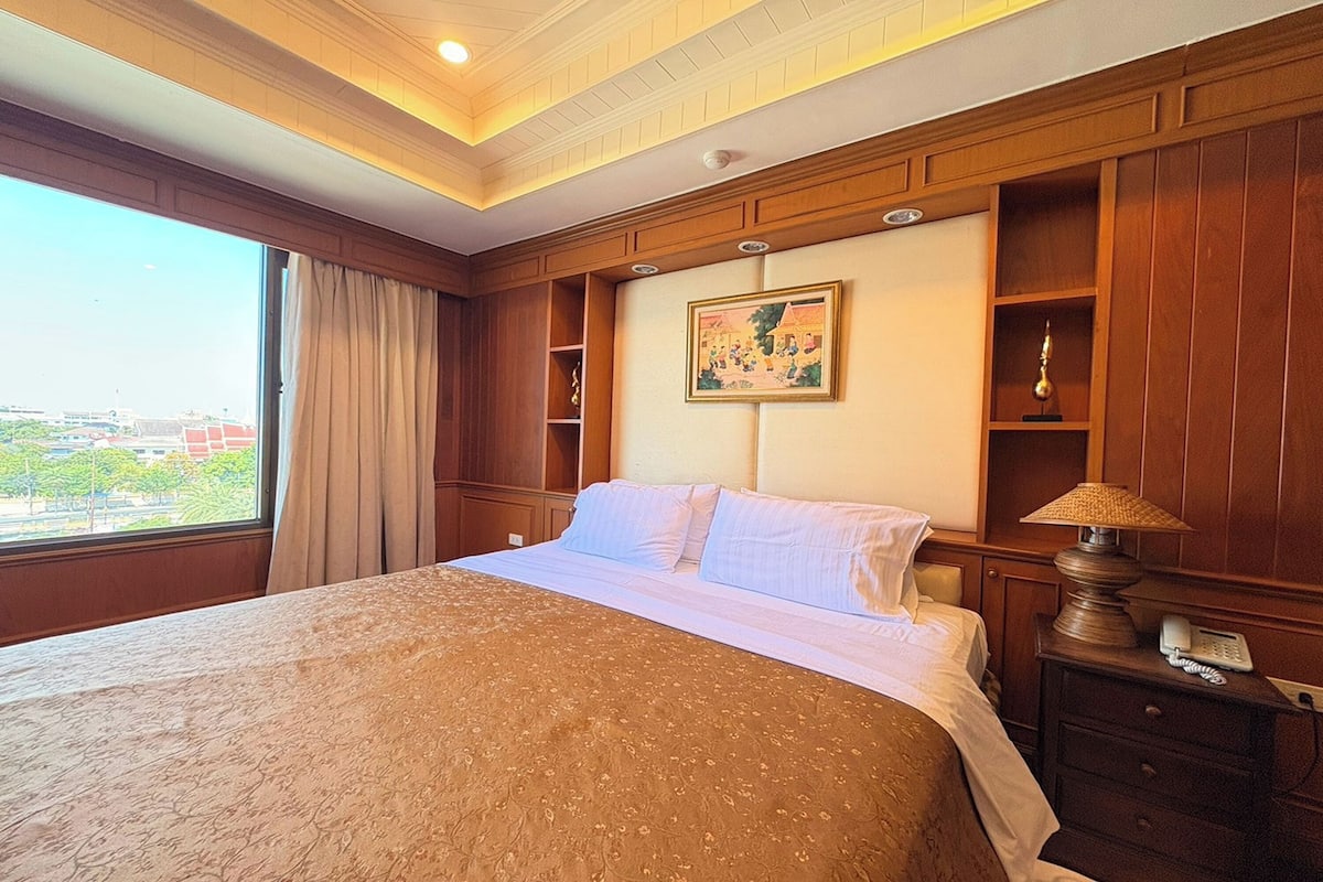 Habitación de hotel con una cama grande, una mesita de noche con lámpara, un cuadro en la pared y una ventana con cortinas.
