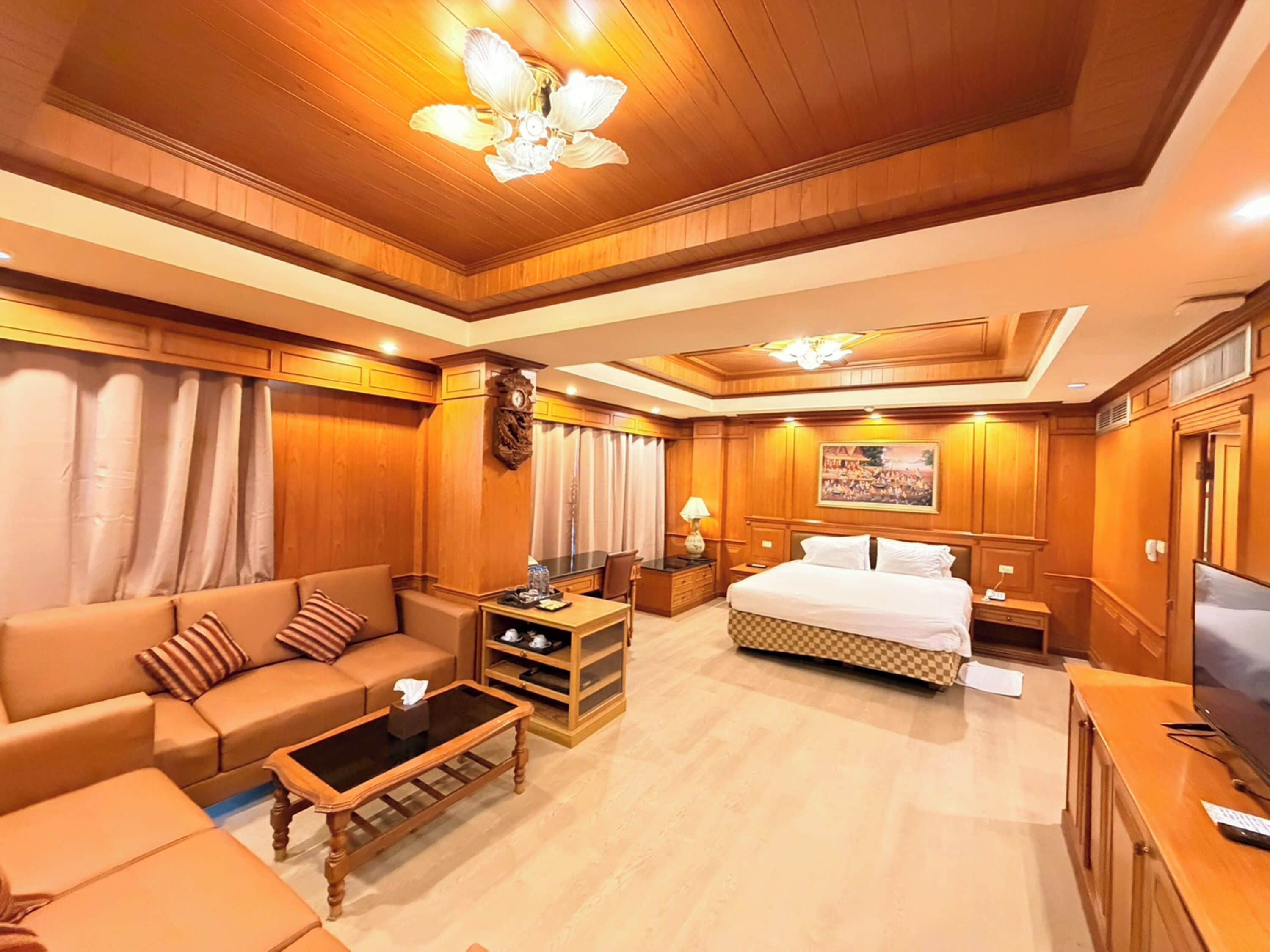 Habitación de hotel con techo de madera, una cama, un sofá, una mesa de centro, un televisor y un cuadro en la pared.