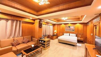 Habitación de hotel con techo de madera, una cama, un sofá, una mesa de centro, un televisor y un cuadro en la pared.