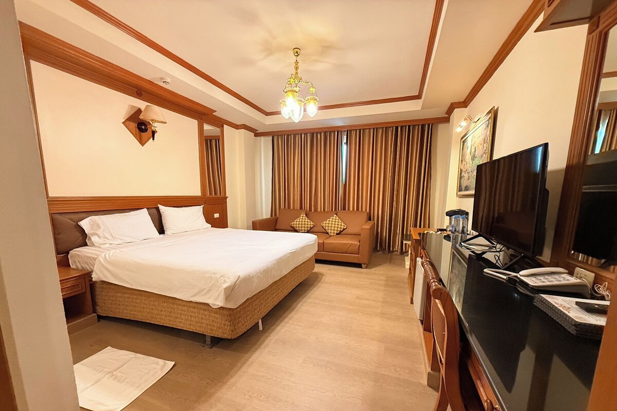 A hotel room with a bed, a sofa, a television, and a desk with a computer.
