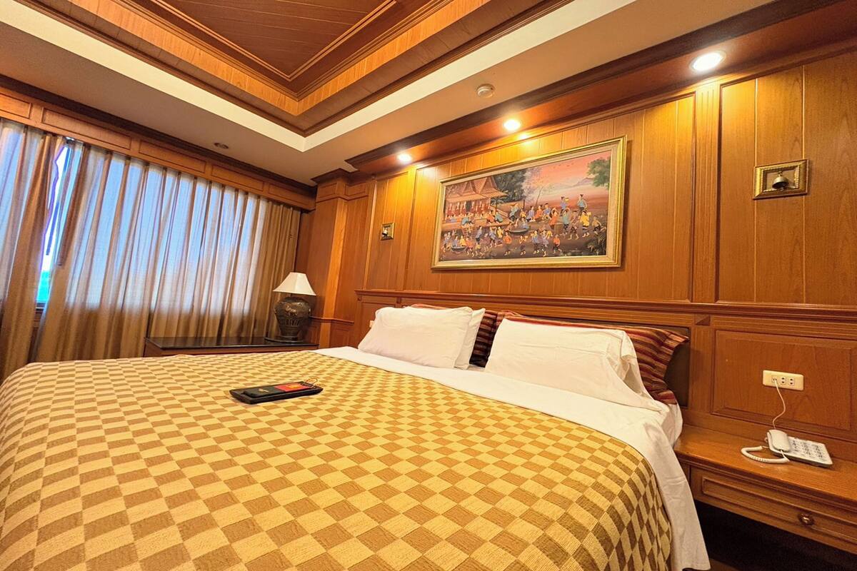 Habitación de hotel con colcha a cuadros, un cuadro sobre la cama, teléfono en la mesita de noche y lámpara.