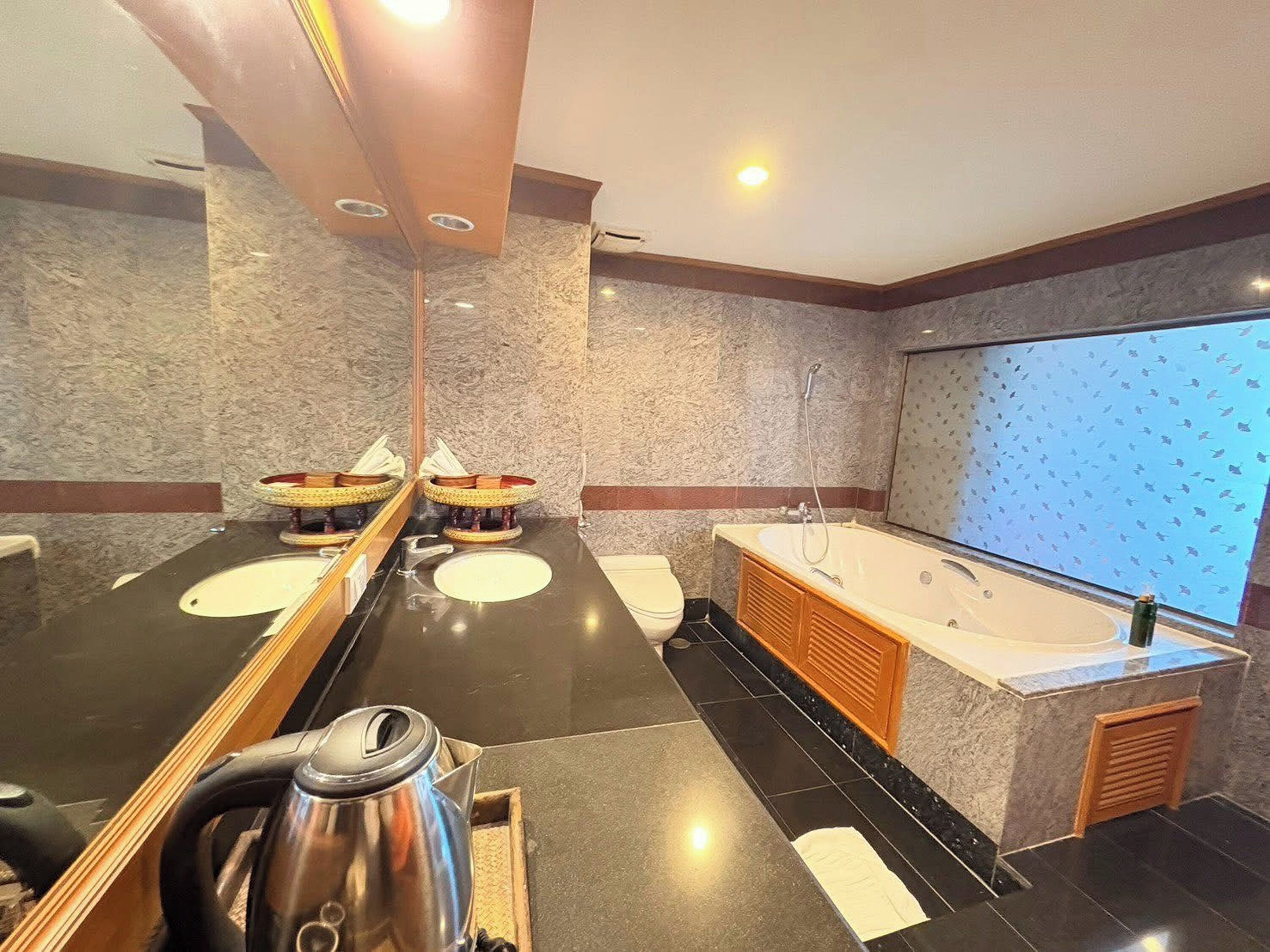 A modern bathroom with a large mirror, two sinks, a bathtub, and a kettle on the counter.
