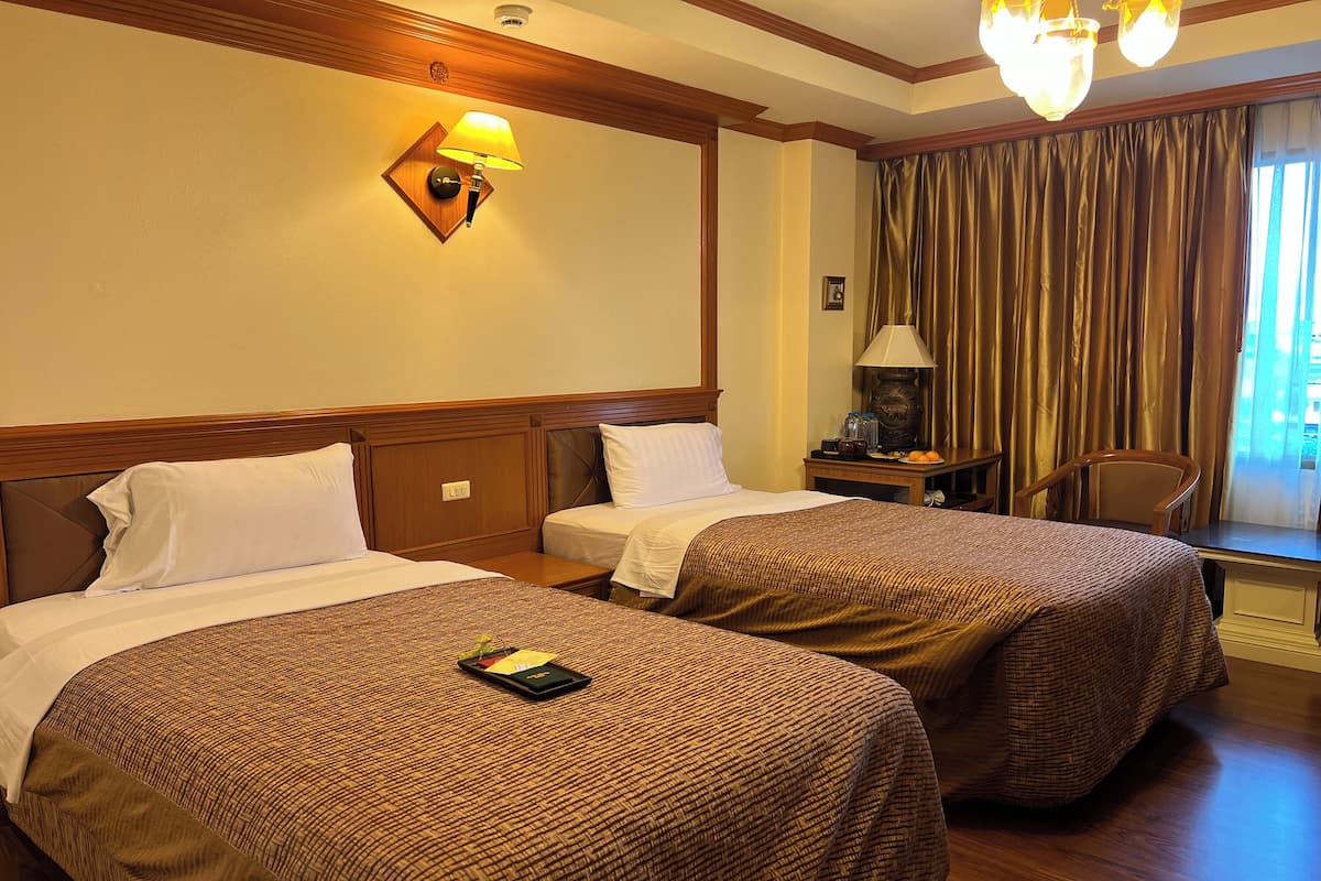 Habitación de hotel con dos camas, una mesita de noche, una lámpara y una ventana con cortinas.