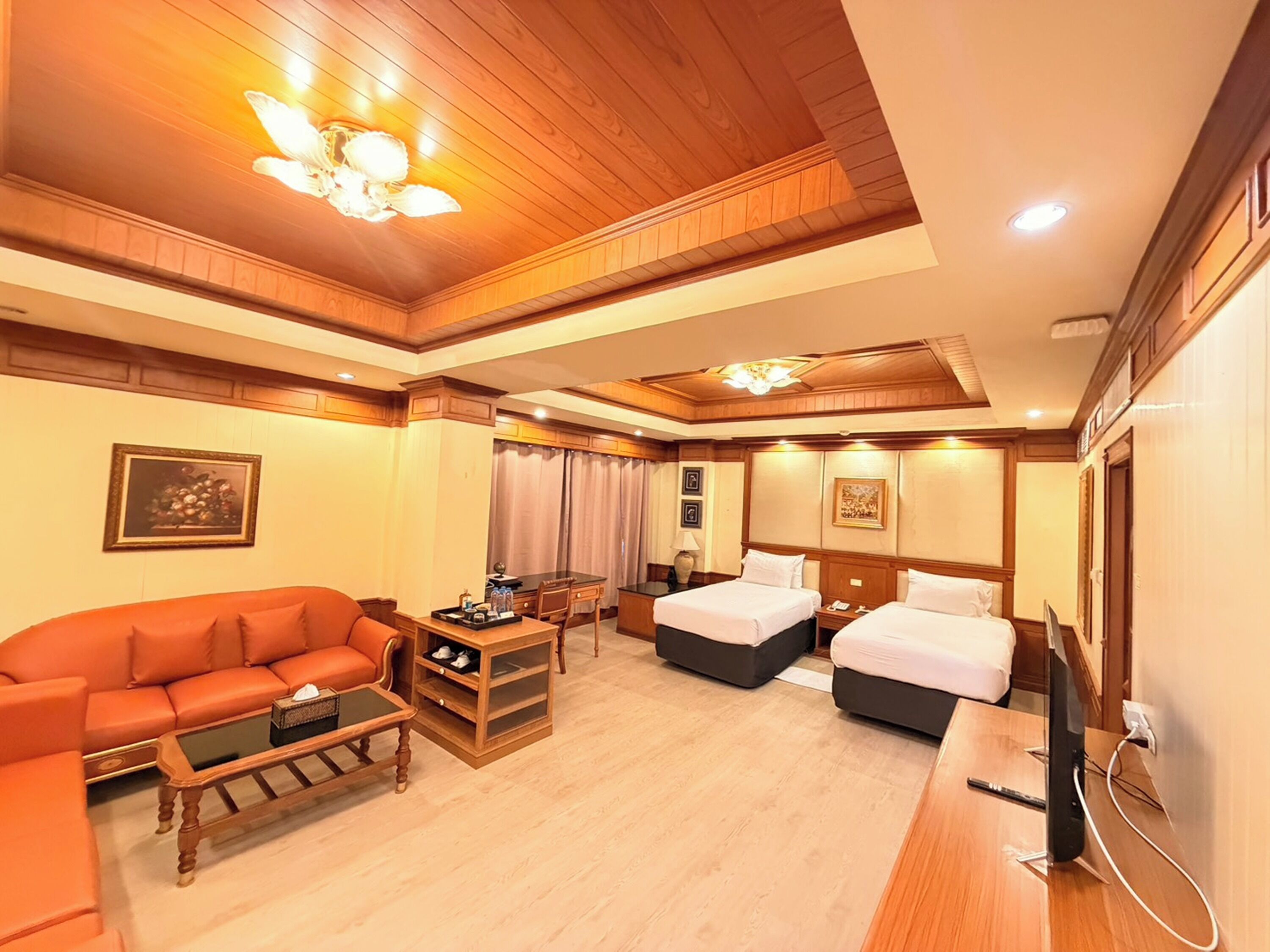 A hotel room with a sofa, two beds, a desk, and a television.